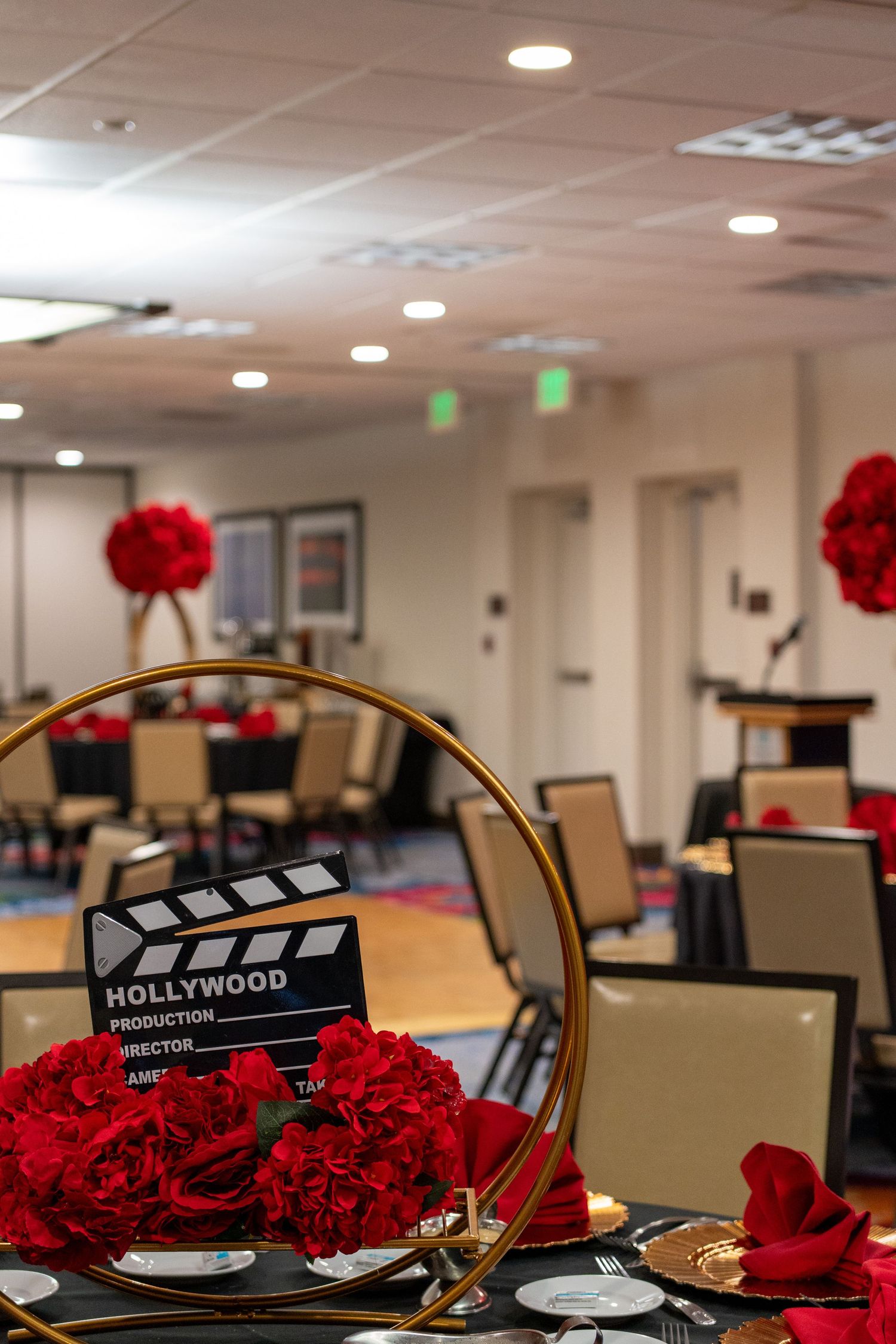 Hollywood-themed event centerpiece with red roses, gold hoop, and clapperboard in a decorated banquet hall.