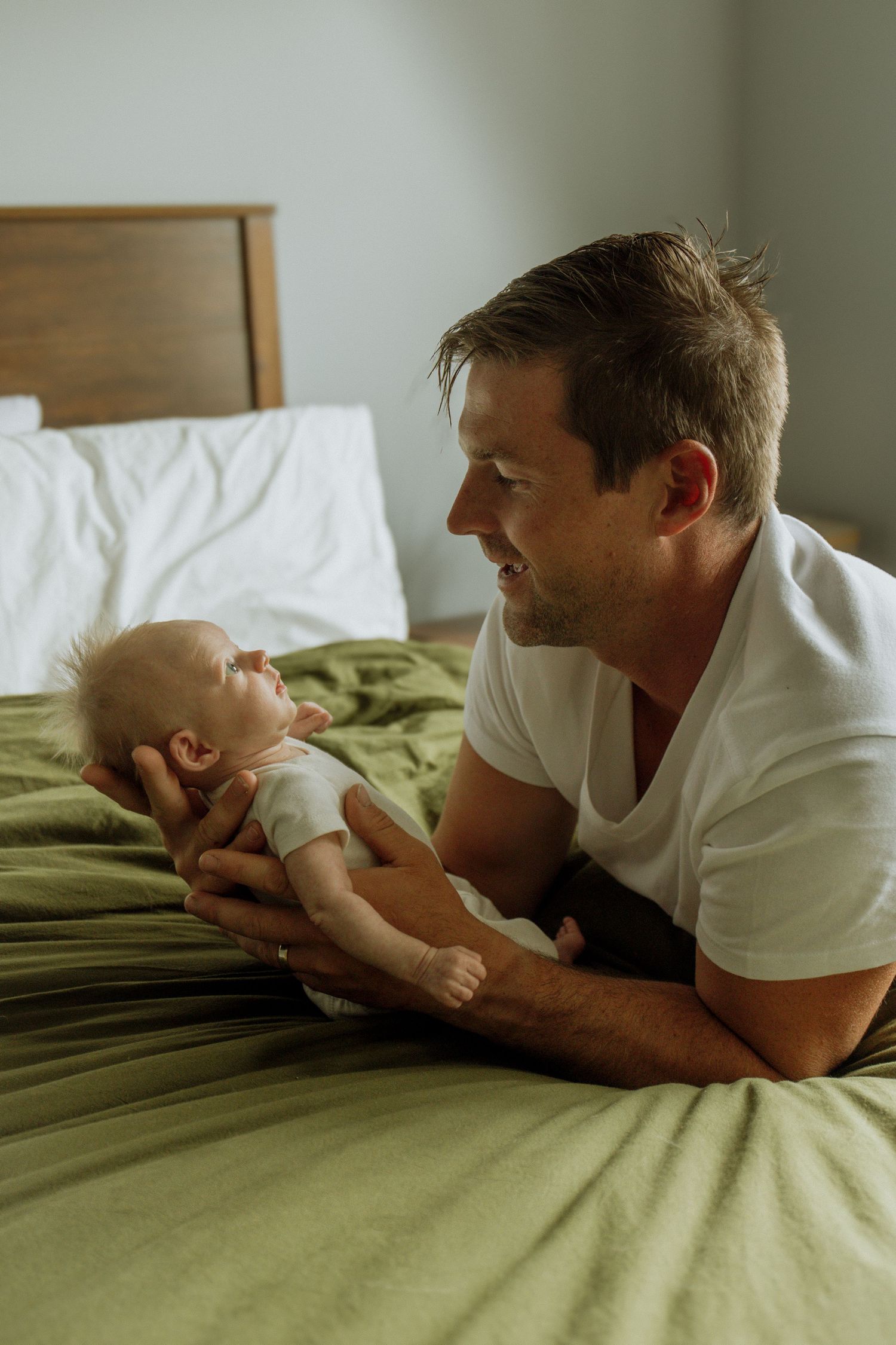 Kawartha Lakes Newborn Photography Session.
Dad holding newborn baby daughter on bed smiling at eachother