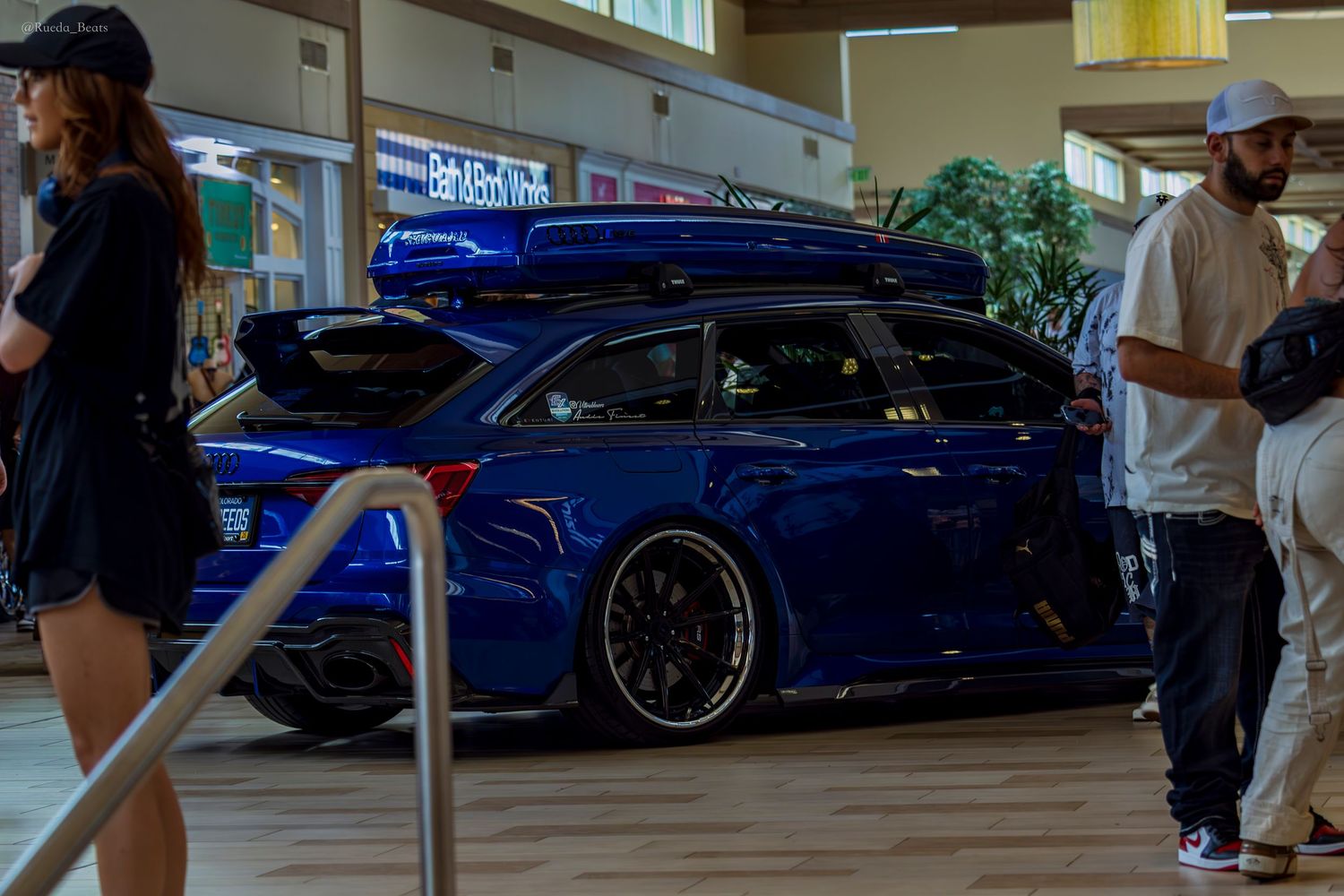 Lowered blue Audi RS6 wagon with roof box and deep dish wheels displayed at indoor mall car show.