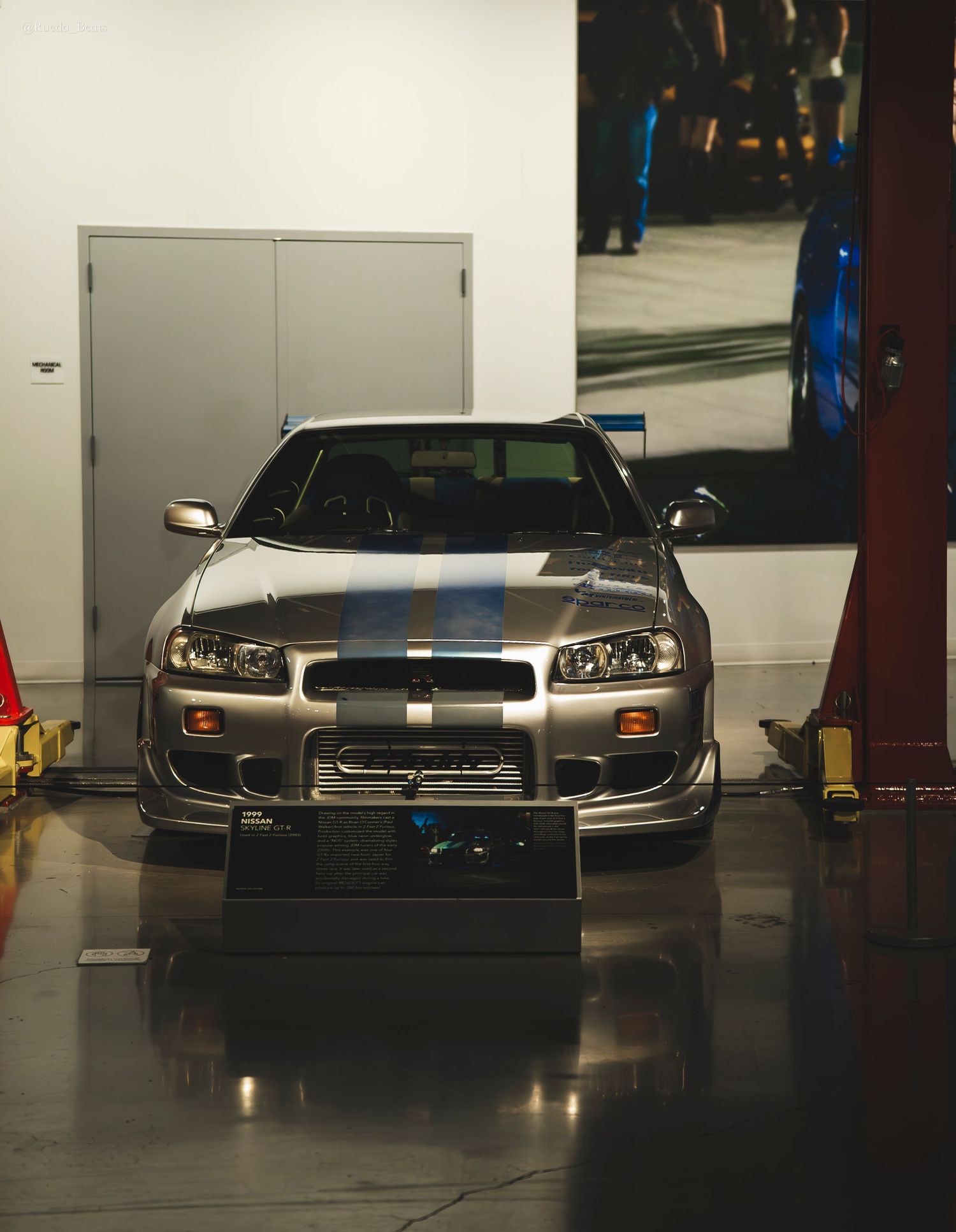 Silver Nissan Skyline GT-R R34 with blue racing stripes on display at Fast and Furious exhibit.