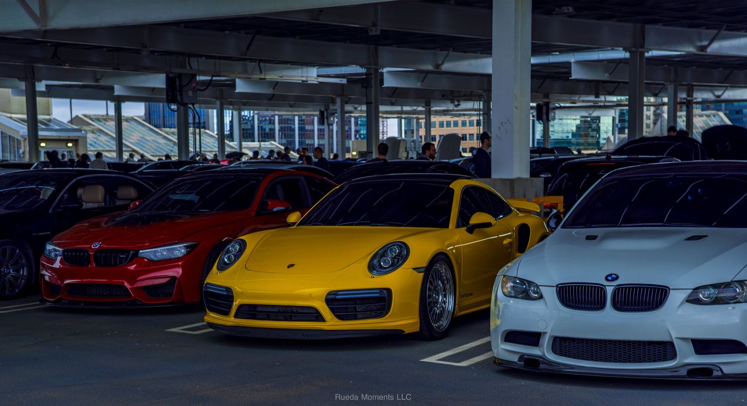 Yellow Porsche 911 Turbo flanked by red and white cars at indoor car show.
