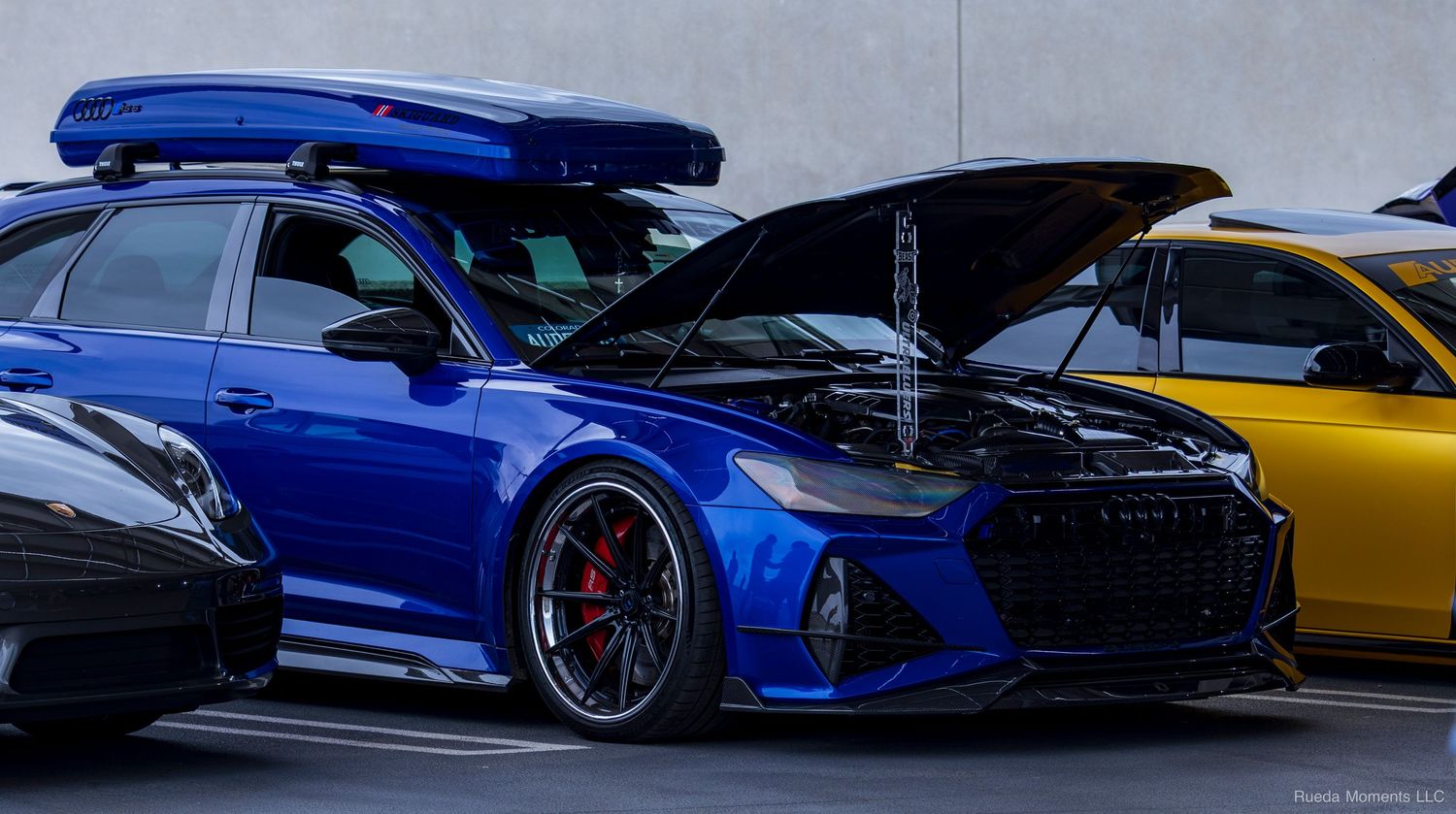 Modified blue Audi RS6 Avant wagon with roof box and open hood at a car show.