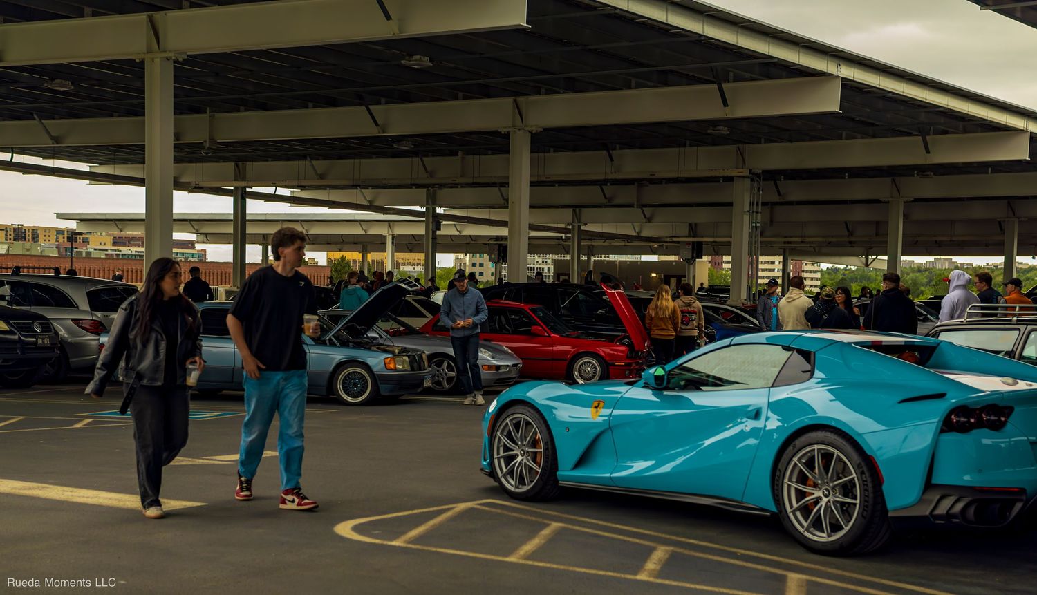 Exotic sports cars including a teal Ferrari on display at an outdoor car show under a covered pavilion.