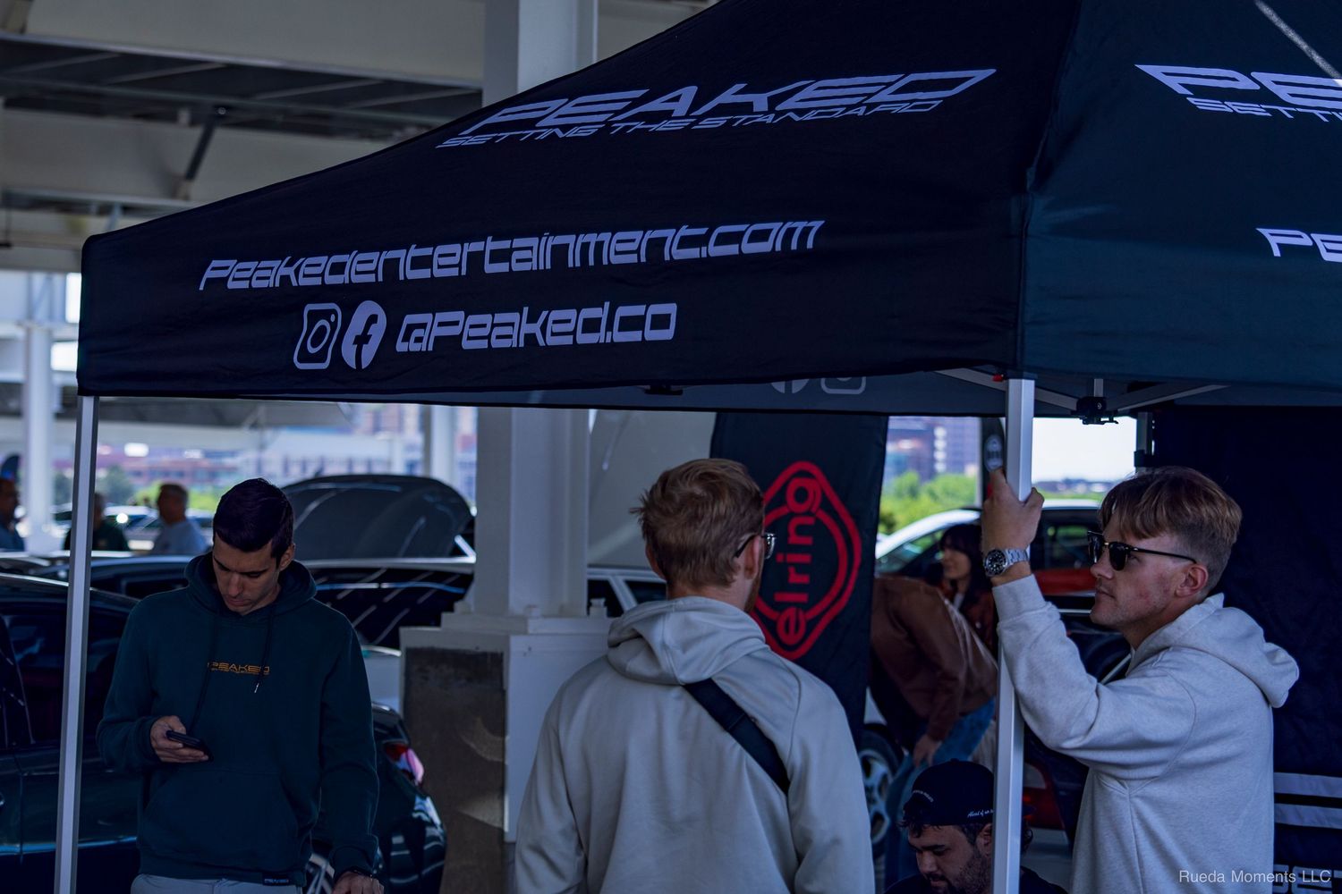Attendees gathered under a GPeaked Entertainment branded canopy tent at an outdoor car event.