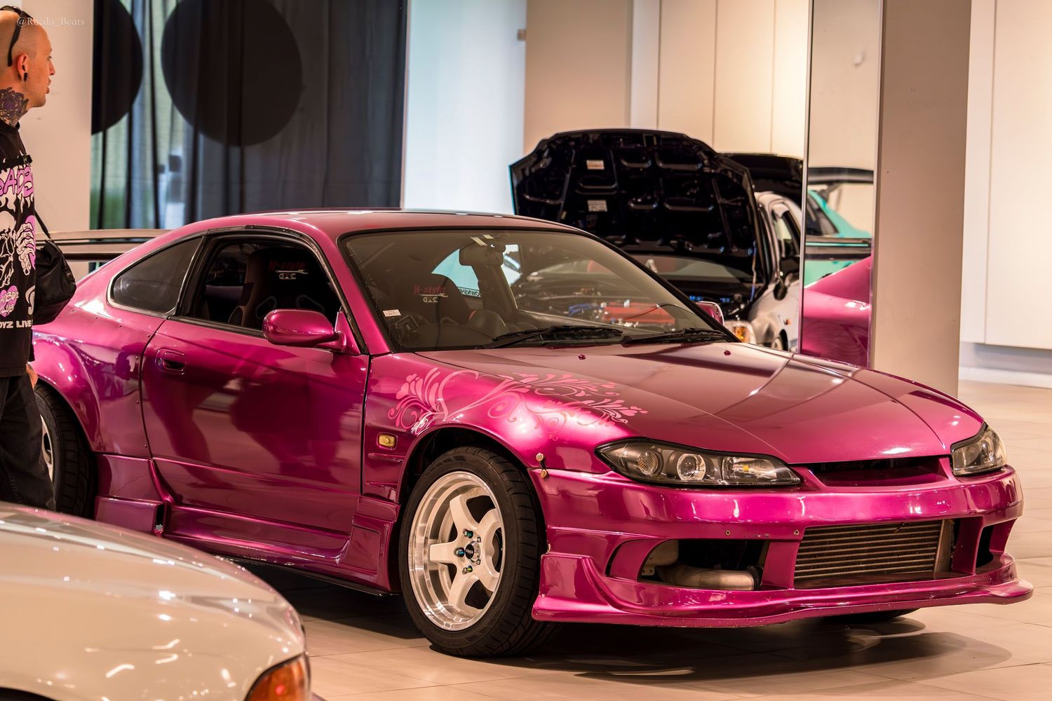 Shiny pink chrome Nissan Silvia S15 widebody on display at an indoor car show event.