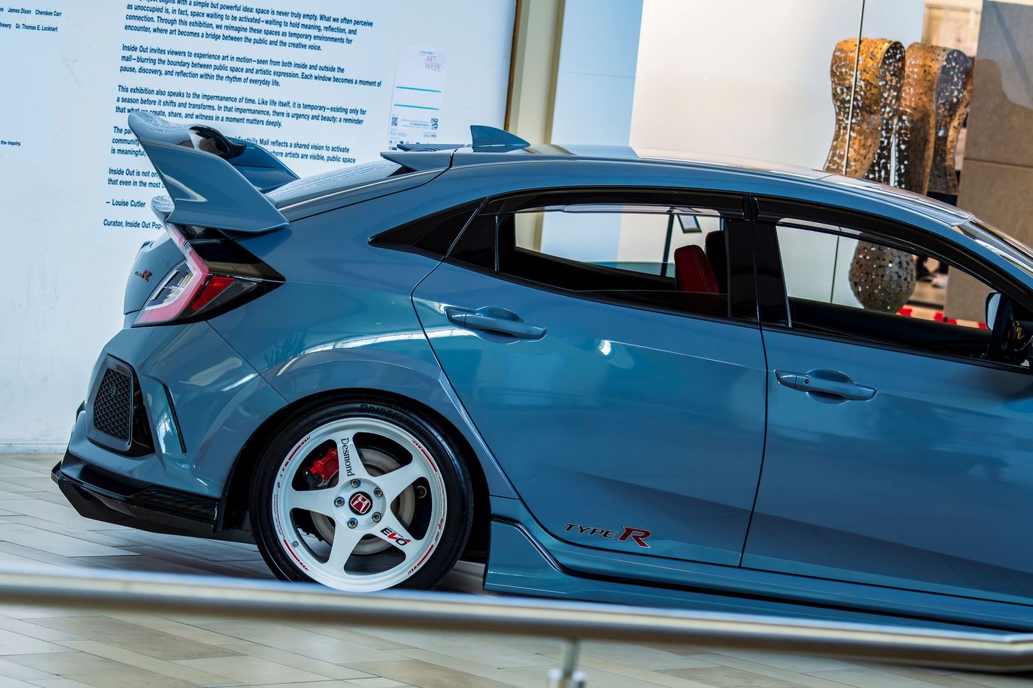 Teal Honda Civic Type R hatchback on display indoors with large rear spoiler.