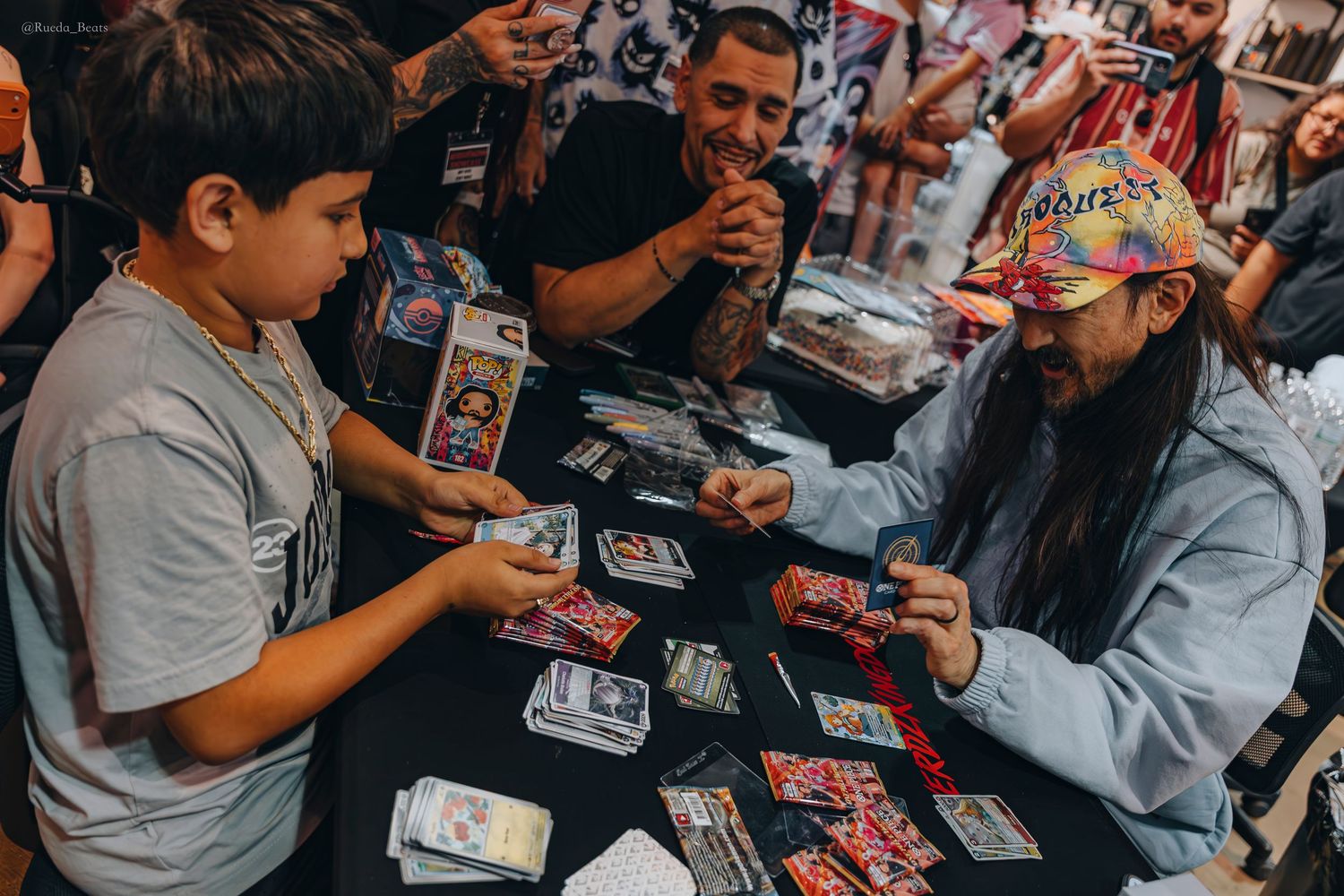 Man in colorful cap signing trading cards for a young boy at an event.