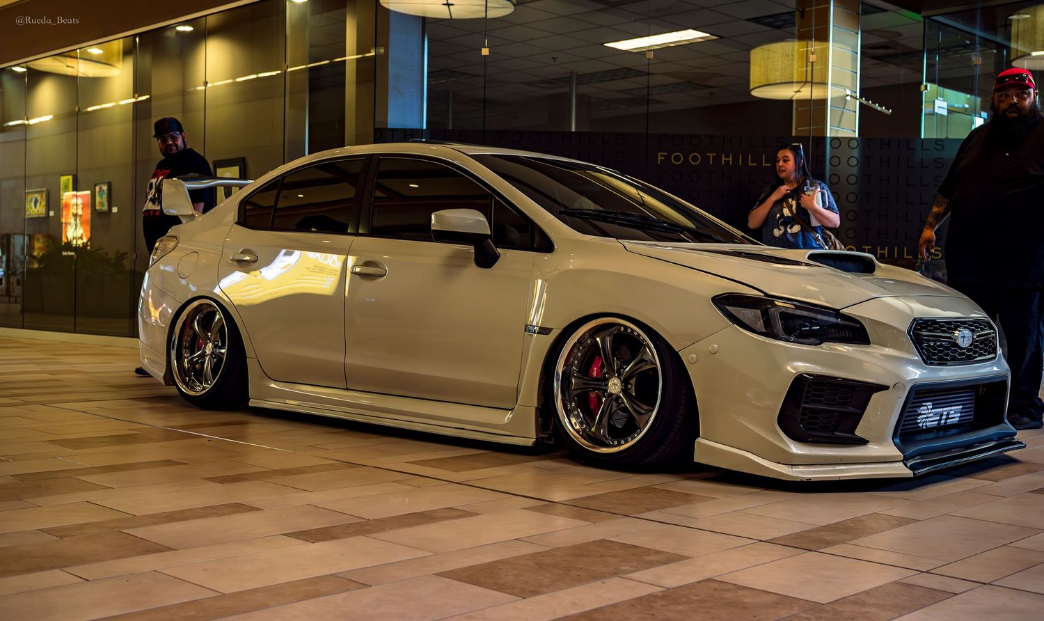 White Subaru WRX STI bagged on black wheels at Foothills mall car show at night.