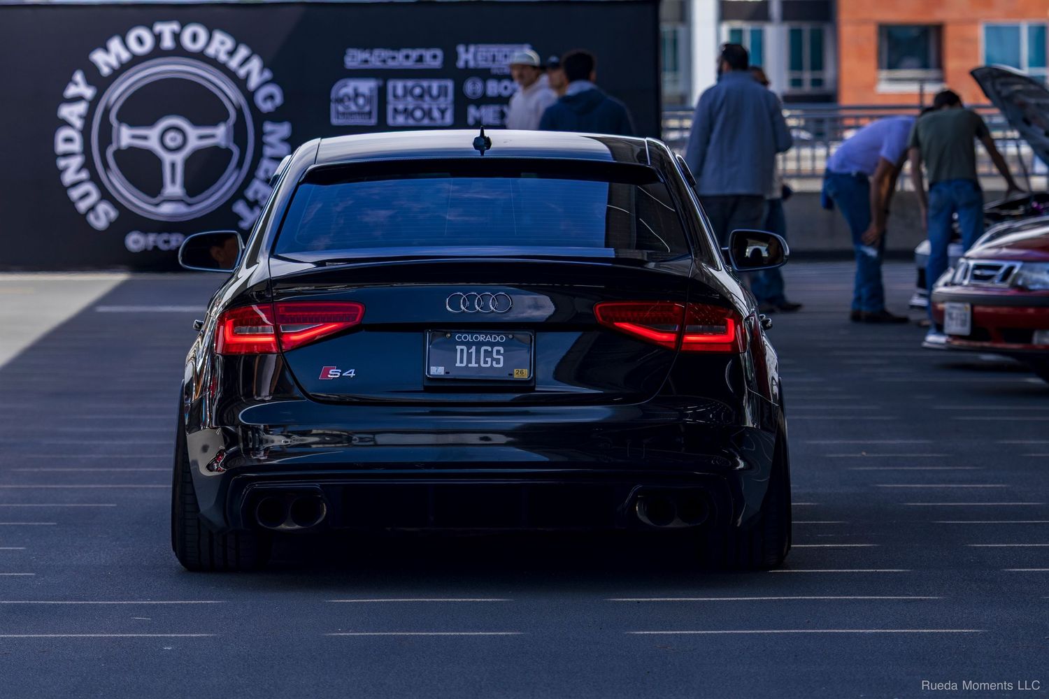 Rear view of a lowered black Audi S4 at Sunday Motoring car meet in a parking lot.