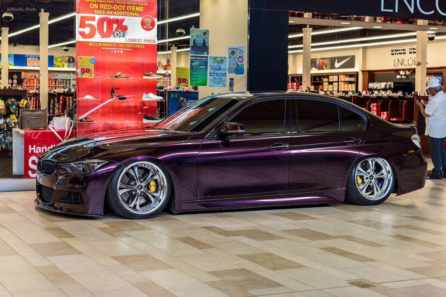 Purple BMW 3 Series slammed on air suspension with chrome wheels at indoor show.