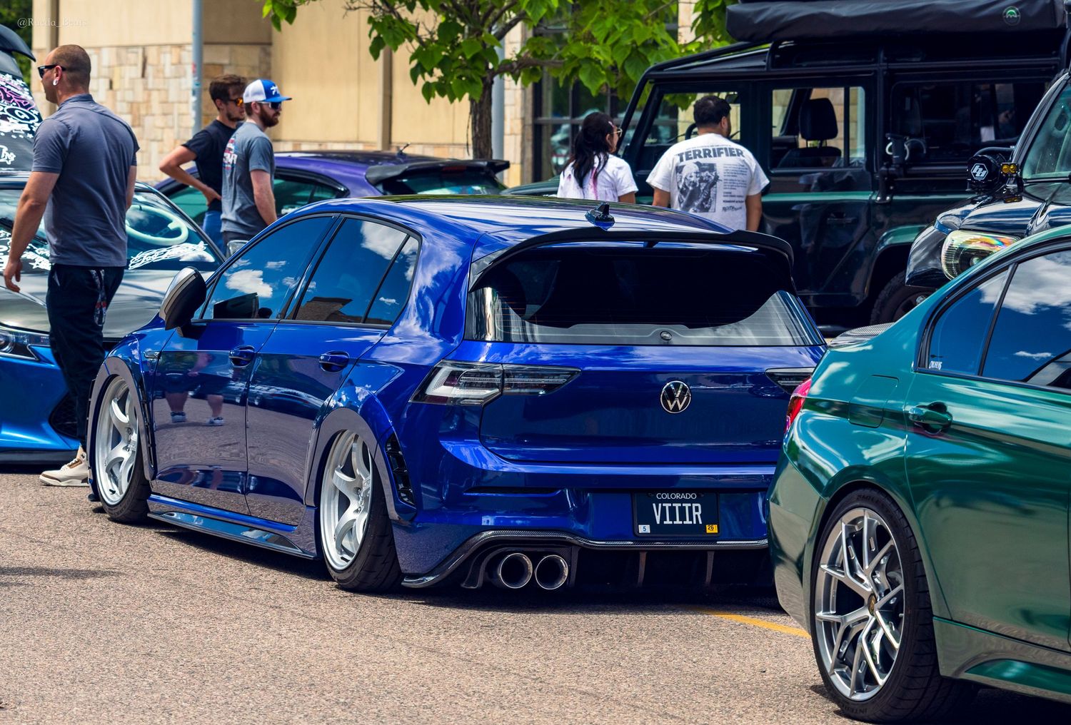 Slammed blue Volkswagen Golf R with custom exhaust at outdoor car show.