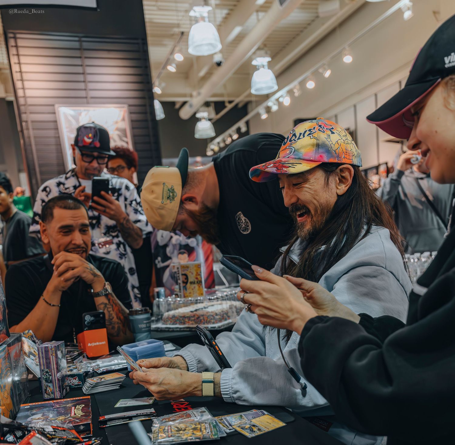 Man in colorful cap reacting excitedly to trading card pull surrounded by fans.