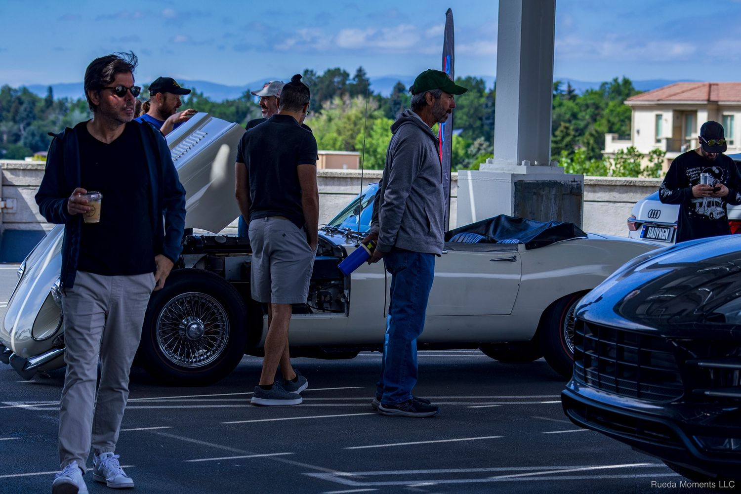 People browse classic and exotic cars at an outdoor car show on a sunny day.