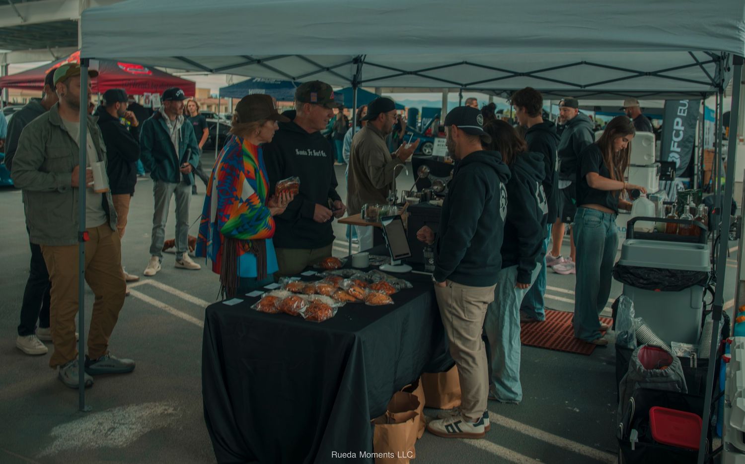 Attendees browsing vendor tables under tents at outdoor car meet.