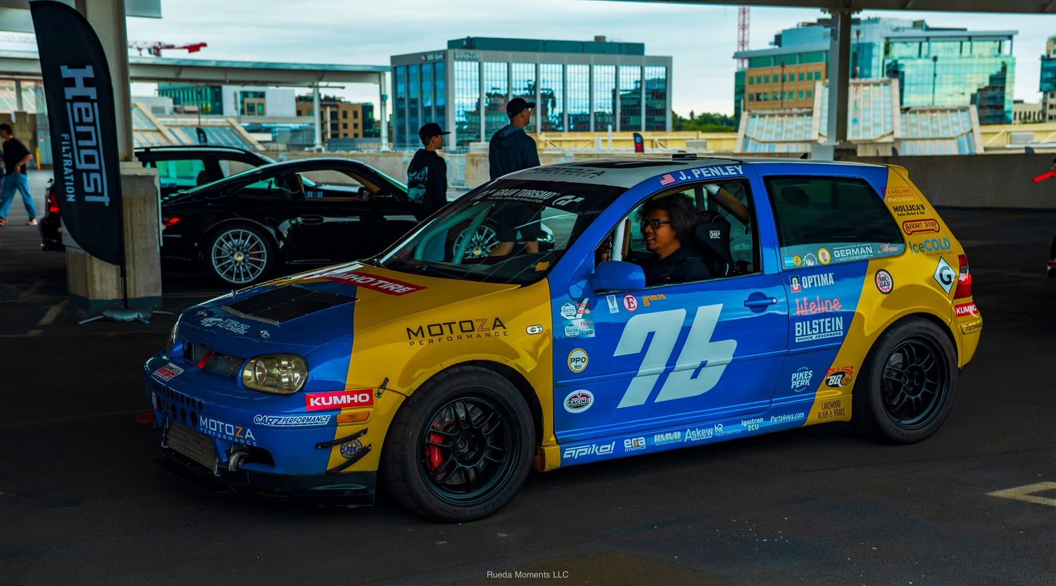 Race-prepped Volkswagen Golf number 76 with colorful livery at an automotive event.