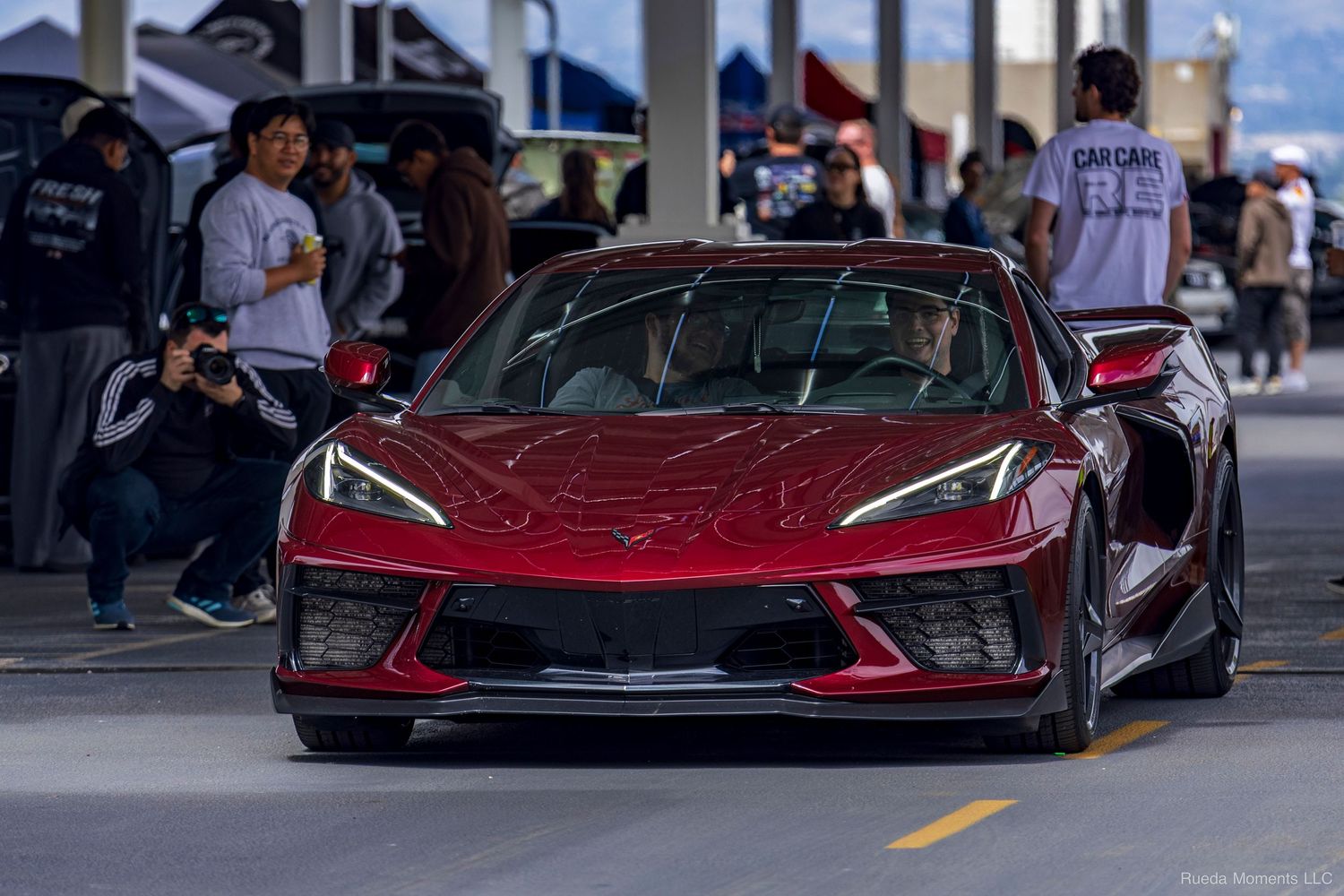Red C8 Chevrolet Corvette Stingray at an outdoor car show surrounded by spectators.