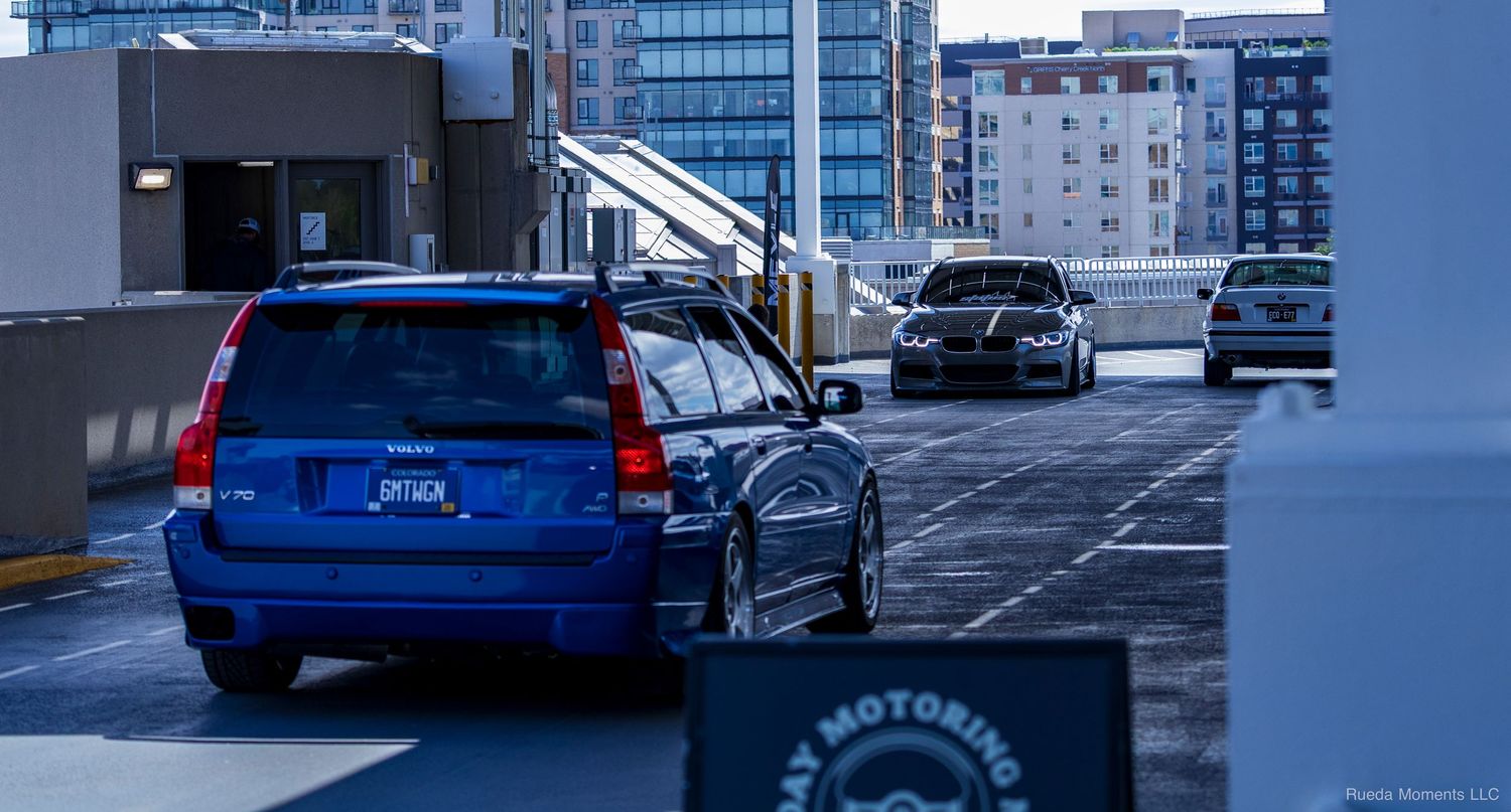 A modified blue Volvo V70 wagon with custom wheels parked in a multilevel parking garage.