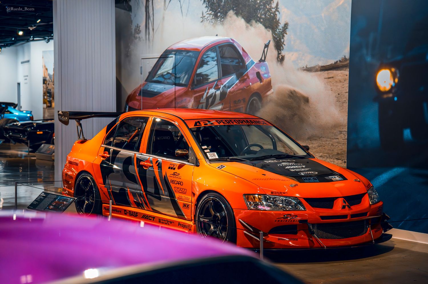 Orange Mitsubishi Lancer Evolution race car with aggressive body kit on museum display.