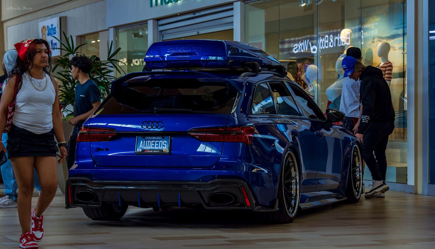 Slammed blue Audi RS6 Avant wagon with roof cargo box and custom plate at indoor shopping mall show.