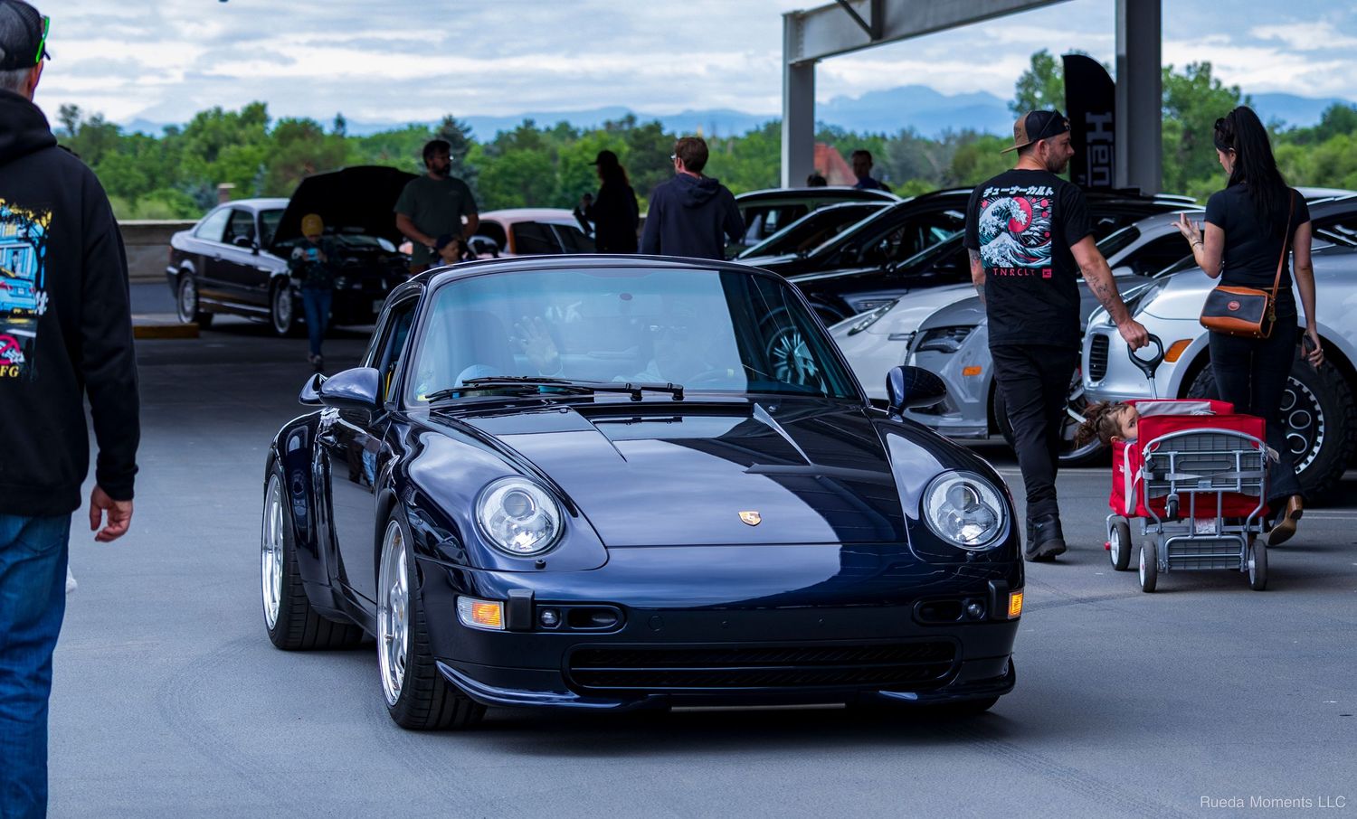 Classic dark blue Porsche 993 parked at an outdoor car show with enthusiasts in background.