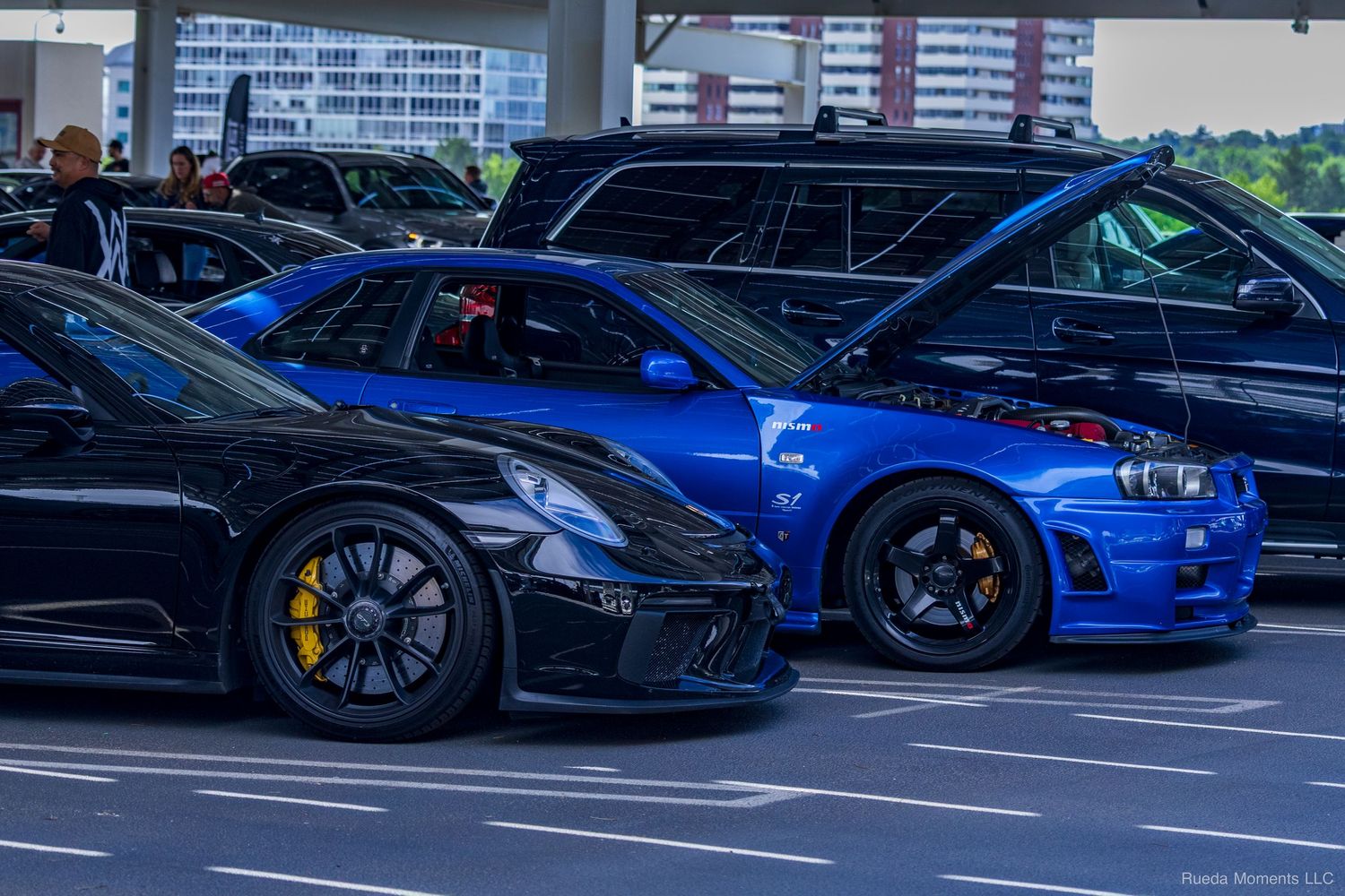 Black Porsche 911 and blue Nissan Skyline GT-R R34 parked side by side at a car meet.