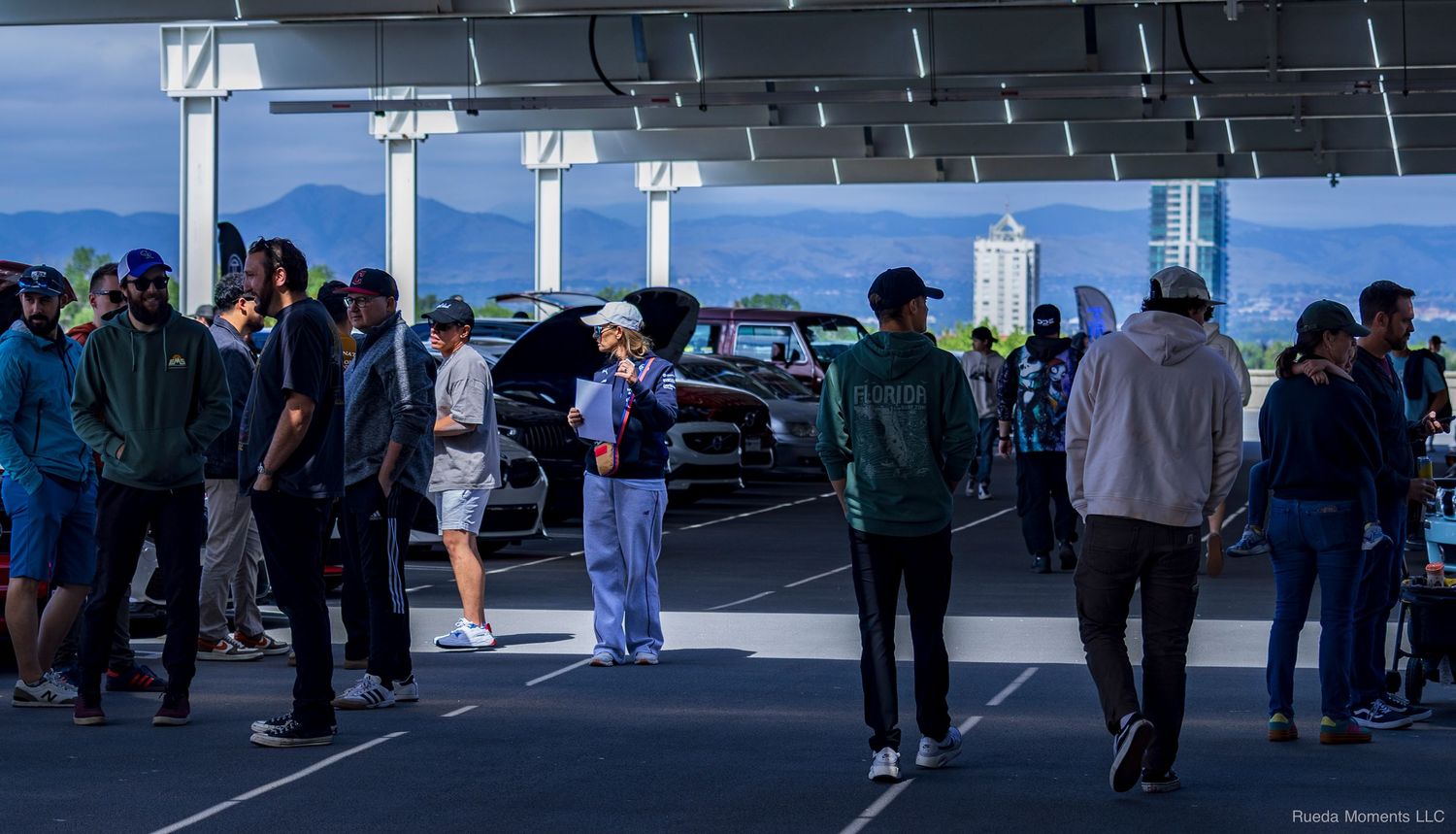 Crowd of automotive enthusiasts gathered under a covered parking structure at a car event.