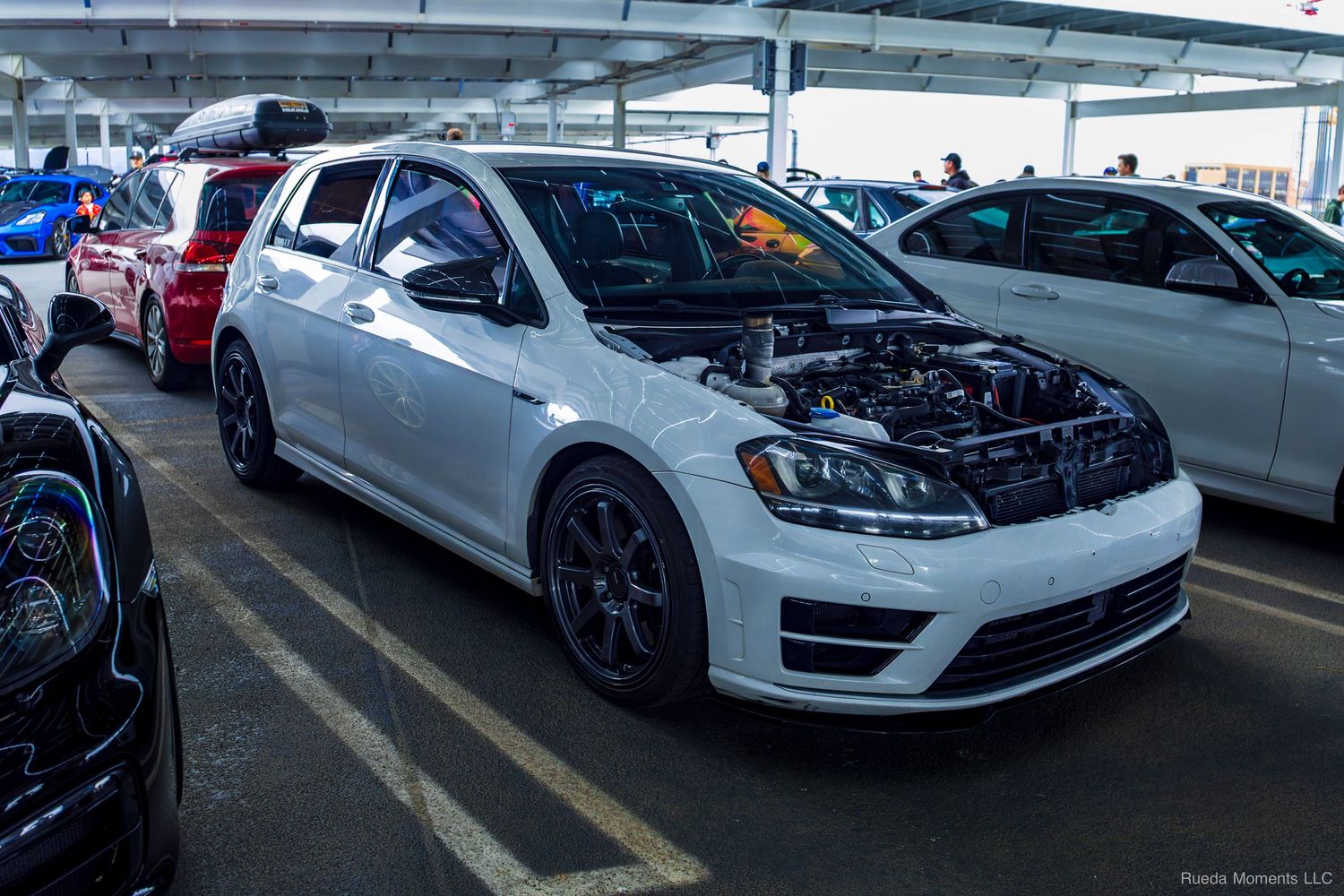 White Volkswagen Golf GTI with open hood on display at a car show.