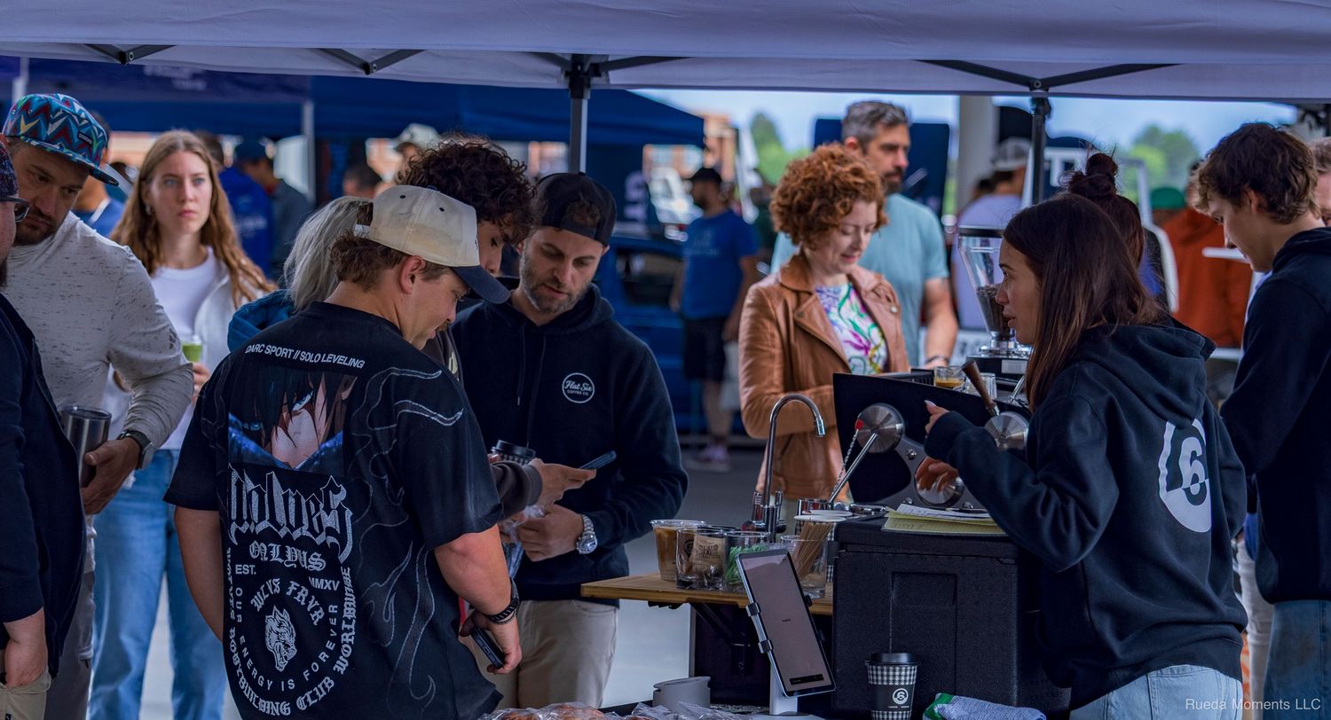 People browsing vendor booths under blue tents at an outdoor automotive event.