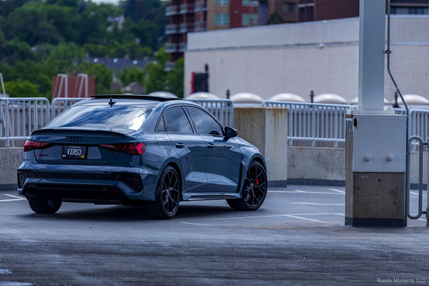 Dark blue Audi RS3 sedan rear view near a parking garage exit.