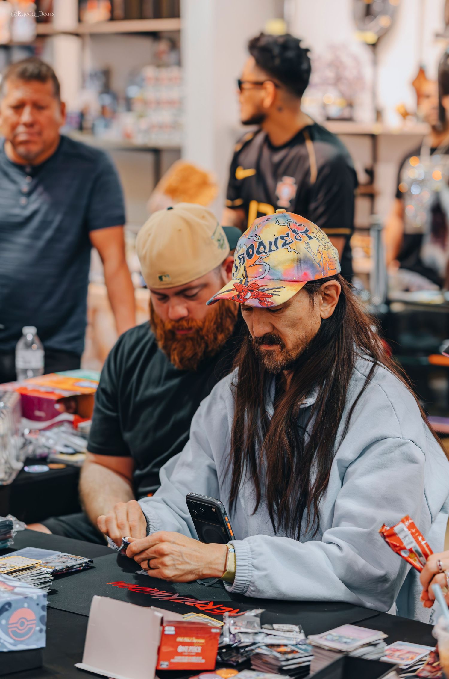 Two men examine trading cards at busy collector event table.