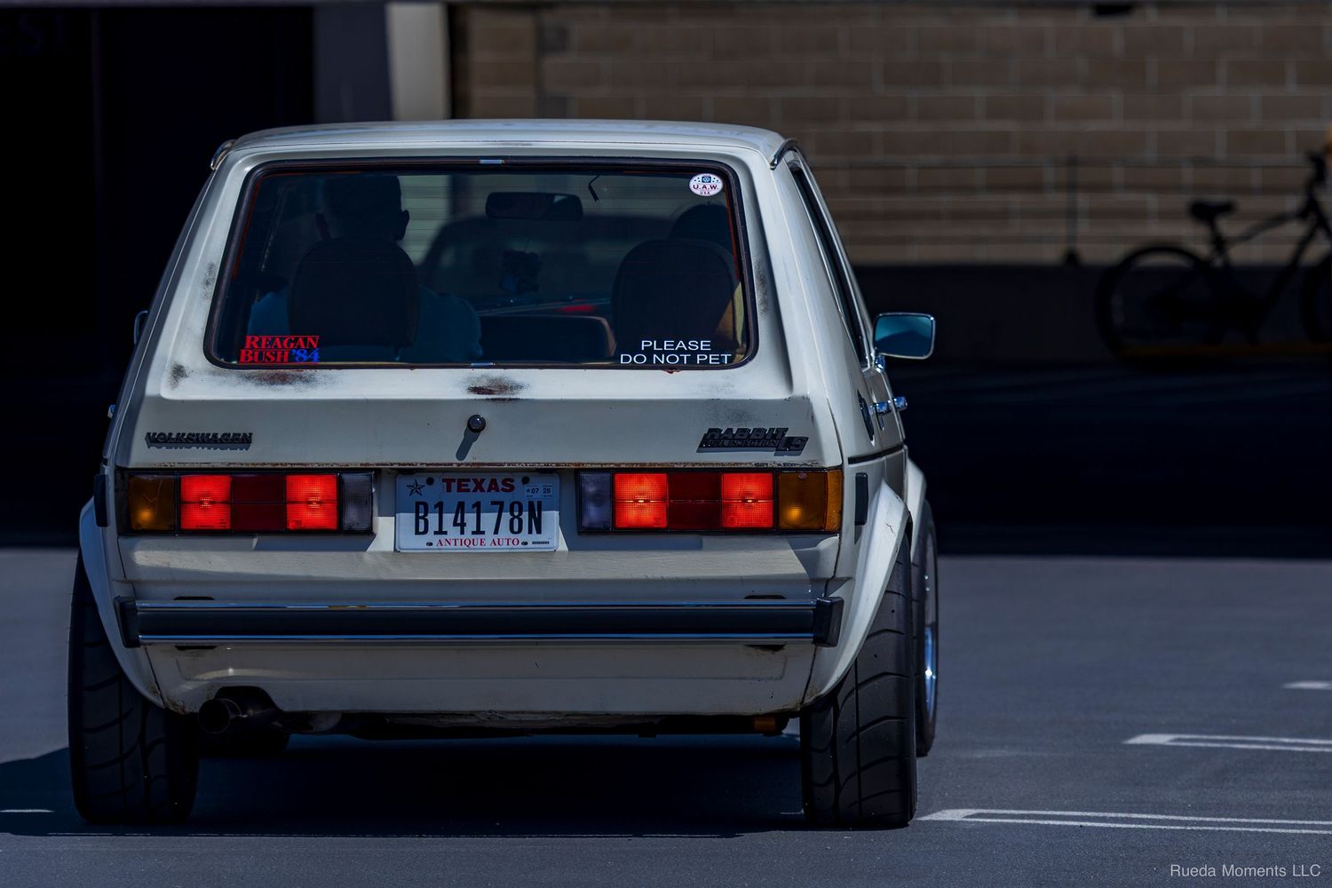 White vintage VW Golf Mk1 rear view with red taillights in a parking lot.