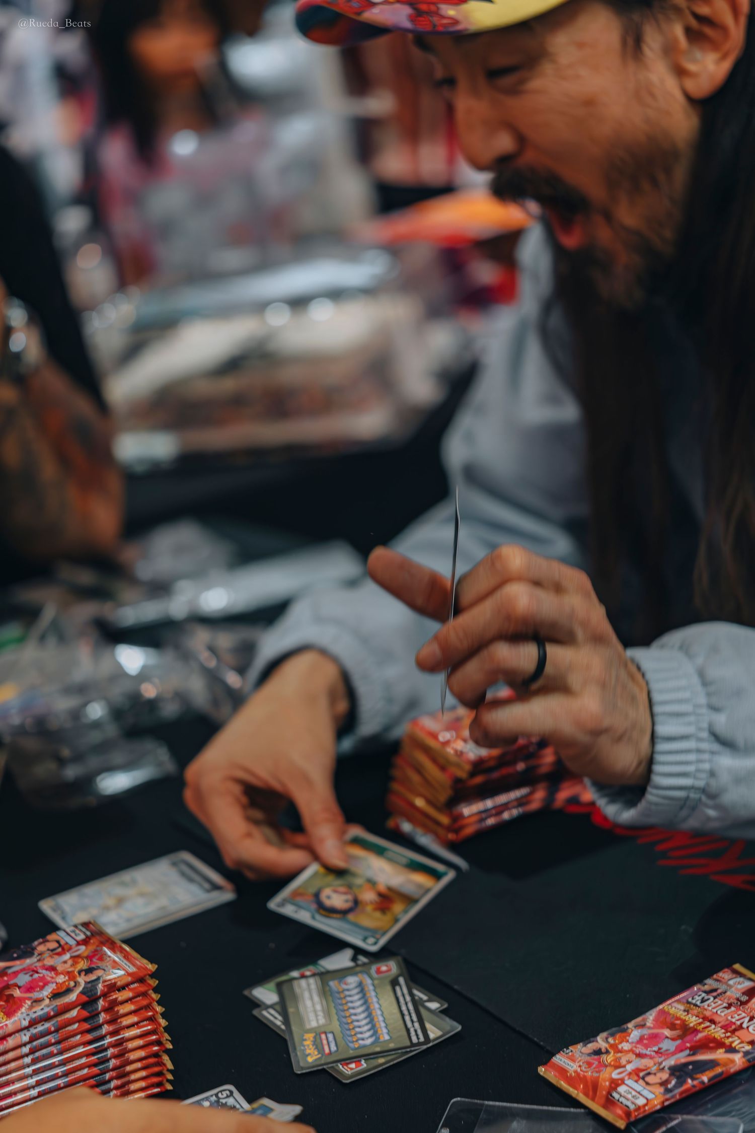 Man in grey hoodie smiling while sorting trading cards at a table.