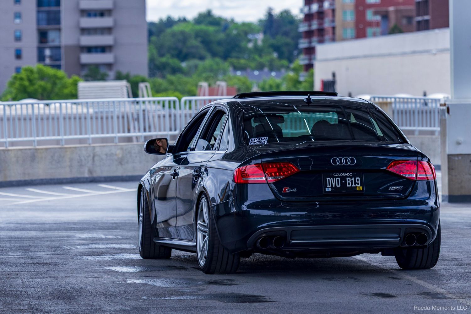 Black Audi RS3 sedan rear view on a wet parking deck.