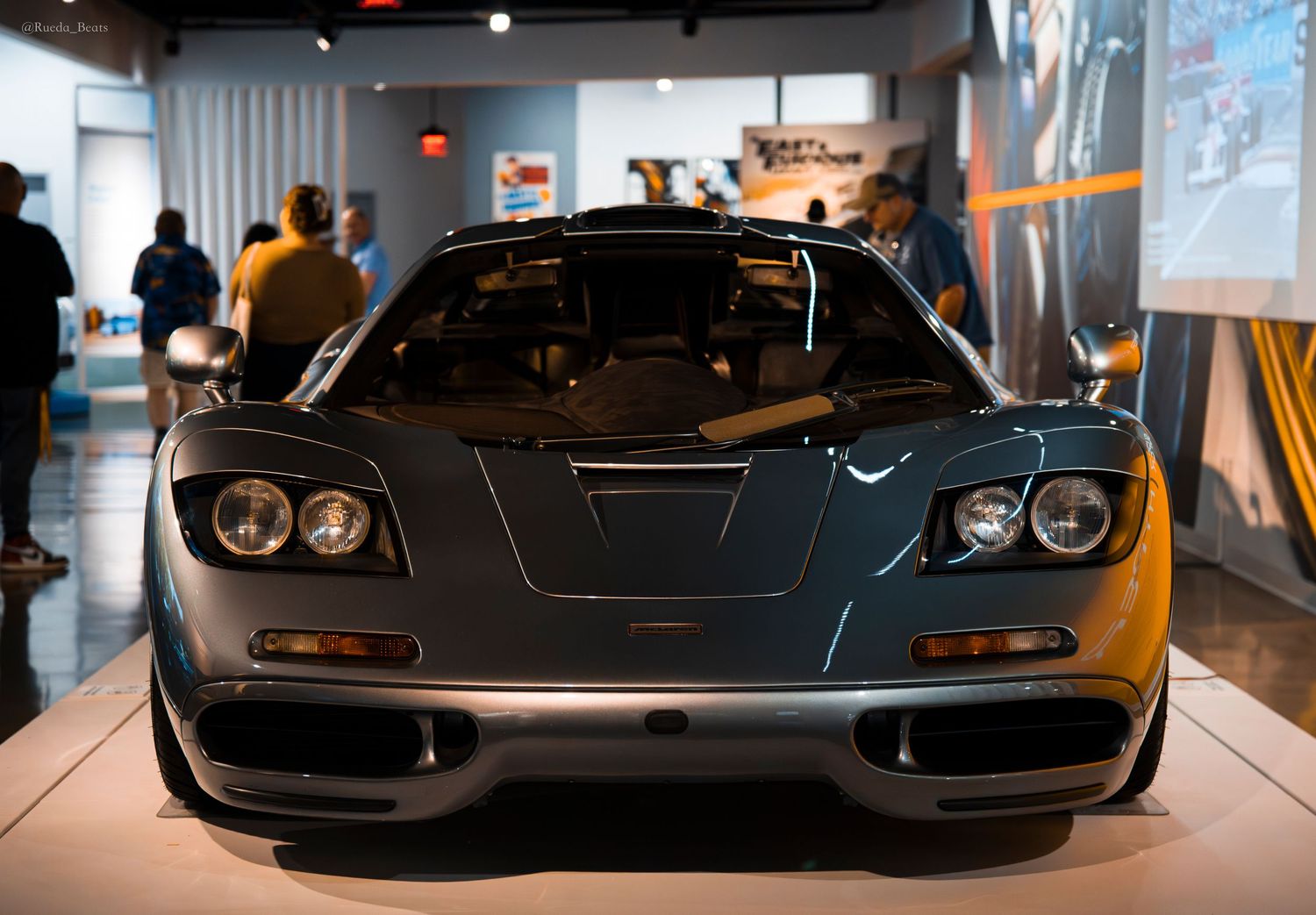 Front view of a McLaren F1 supercar in dark teal displayed in an automotive museum exhibit.
