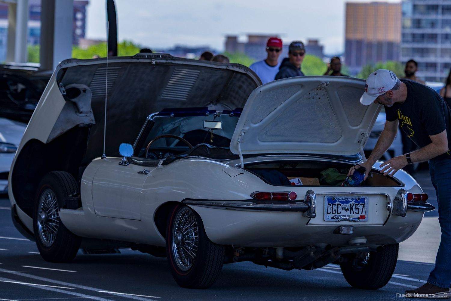 Classic cream white Jaguar E-Type with open hood and trunk on display at an outdoor car show.