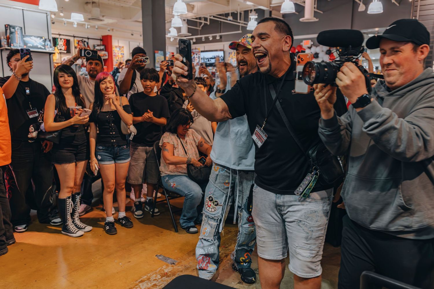 Excited crowd cheering around a man at an indoor event with cameras.