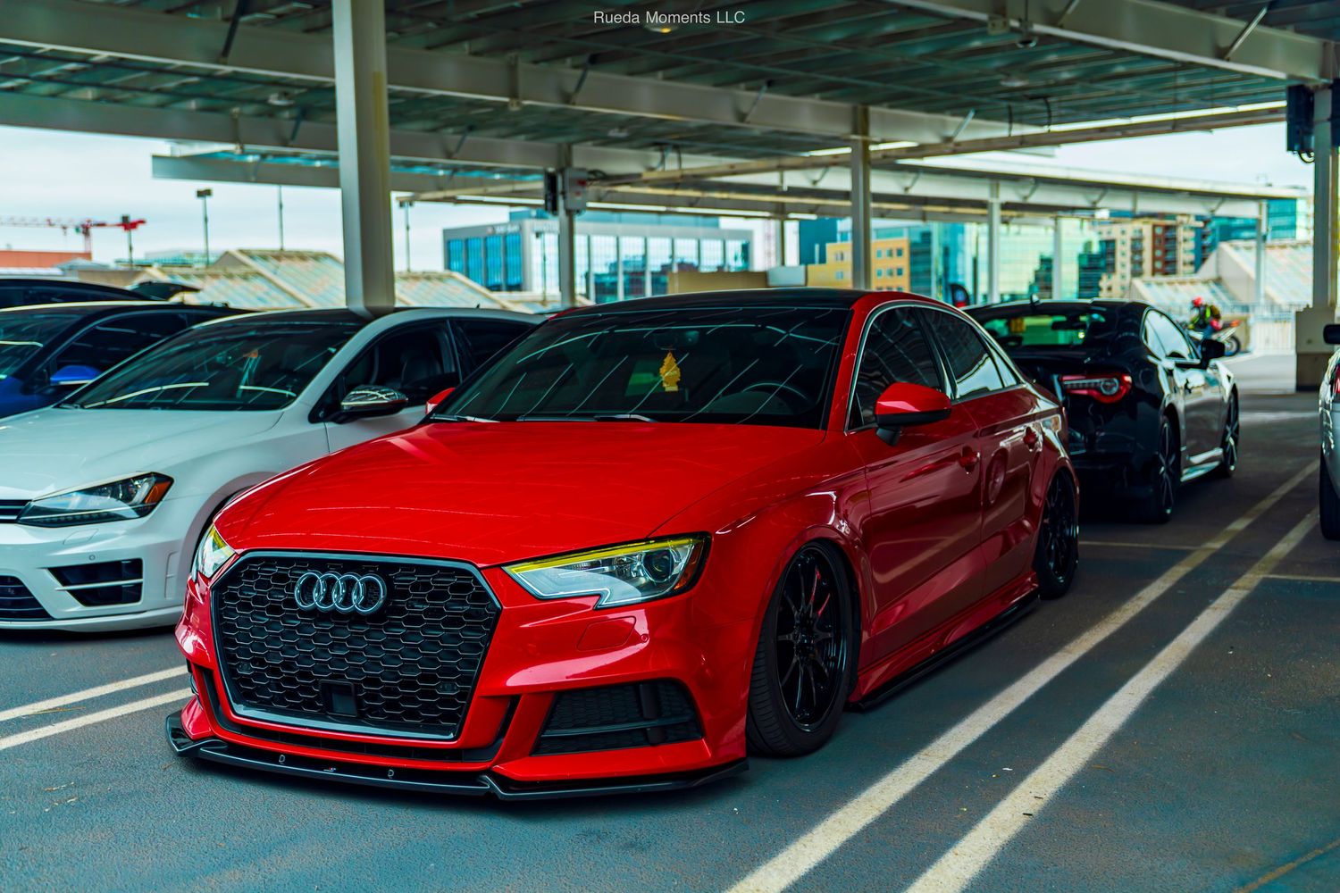 Modified red Audi S3 with aggressive front lip and lowered stance at a car meet.