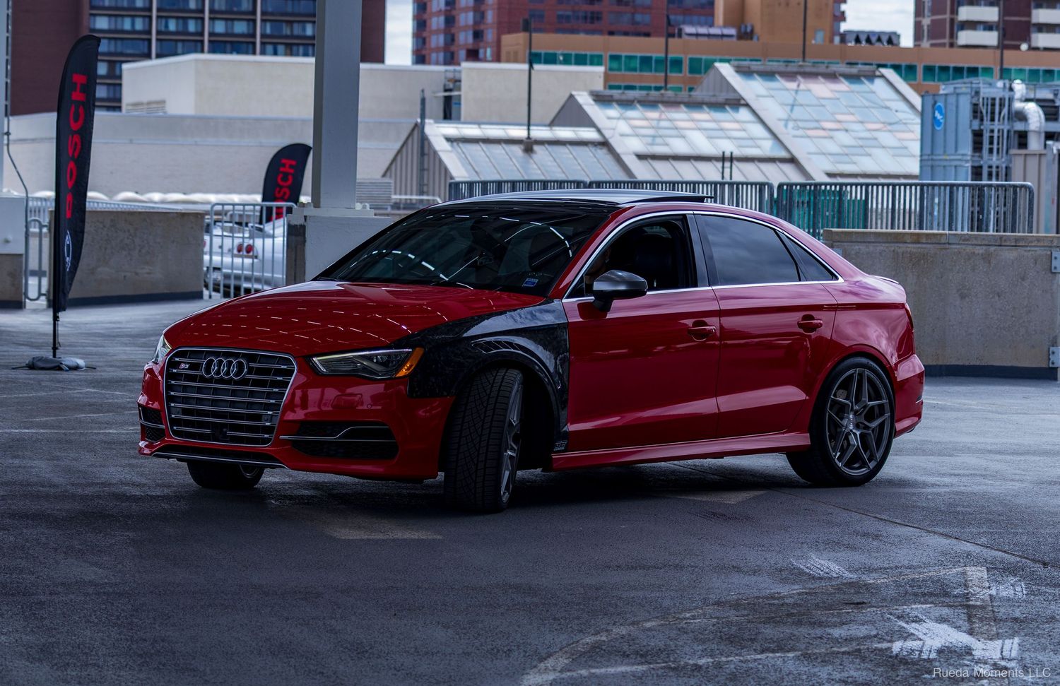A red Audi S3 sedan with lowered suspension and dark wheels parked in an urban garage.