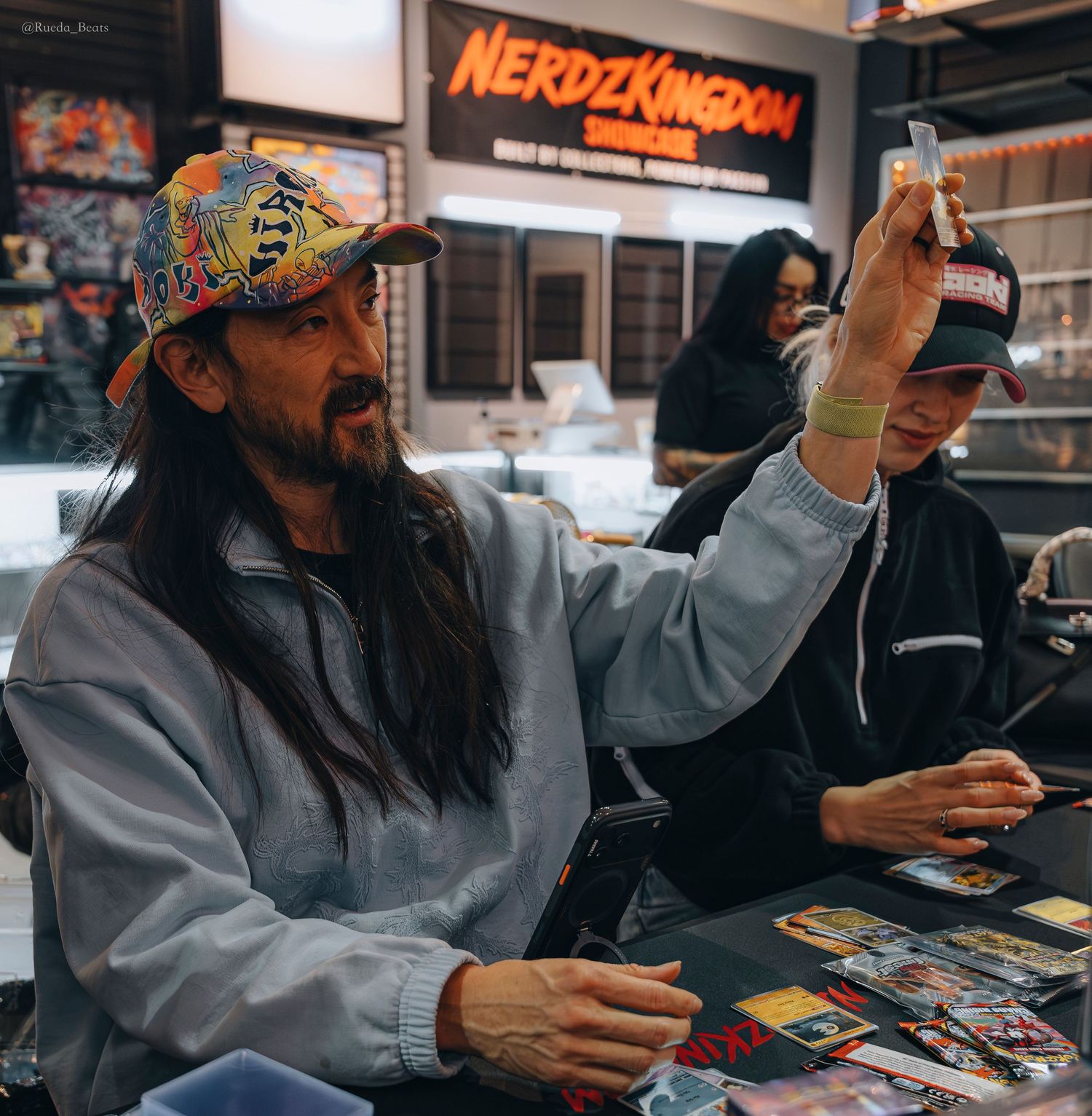 Man holding up trading card at Nerdz Kingdom collectibles store event.