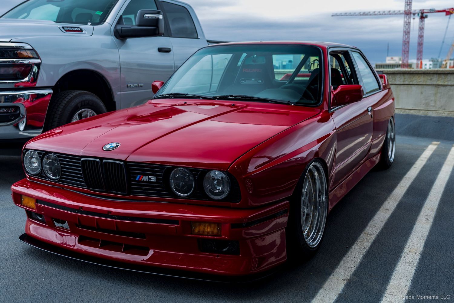 Red BMW E30 M3 with wide body kit and BBS wheels at a car show.