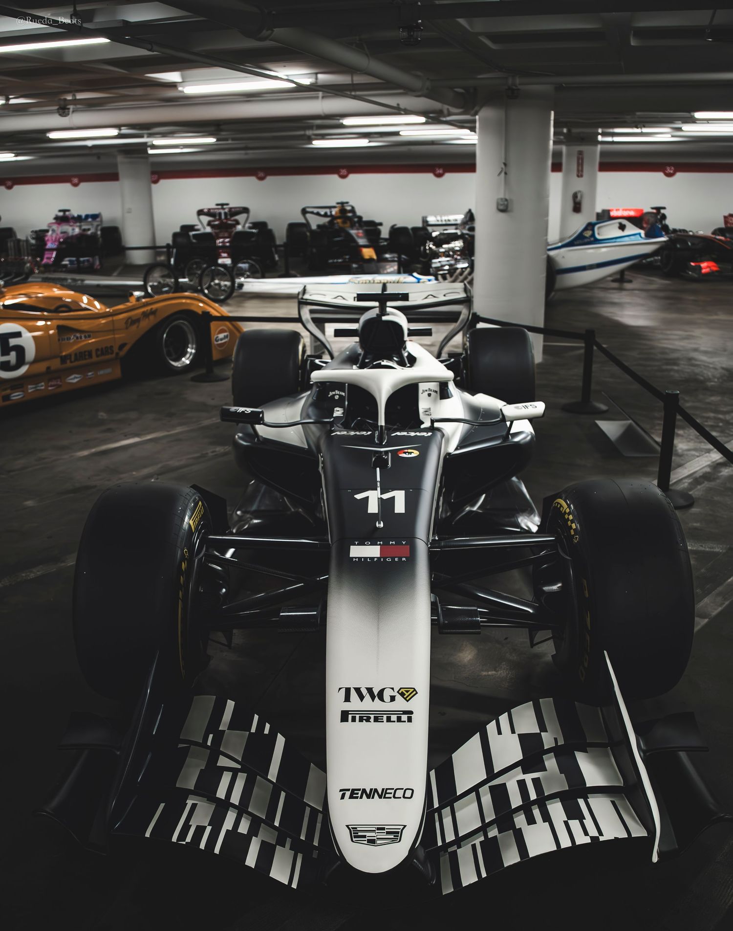 White Formula 1 race car number 11 with TWG and Pirelli sponsors parked in an underground garage.
