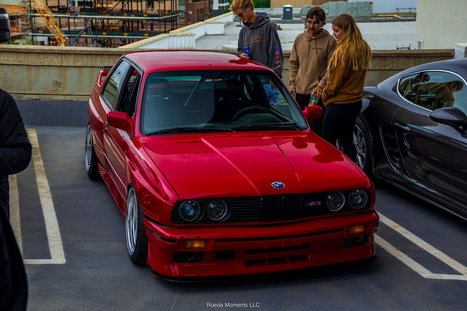 Classic red BMW E30 M3 with period-correct styling at car meet.