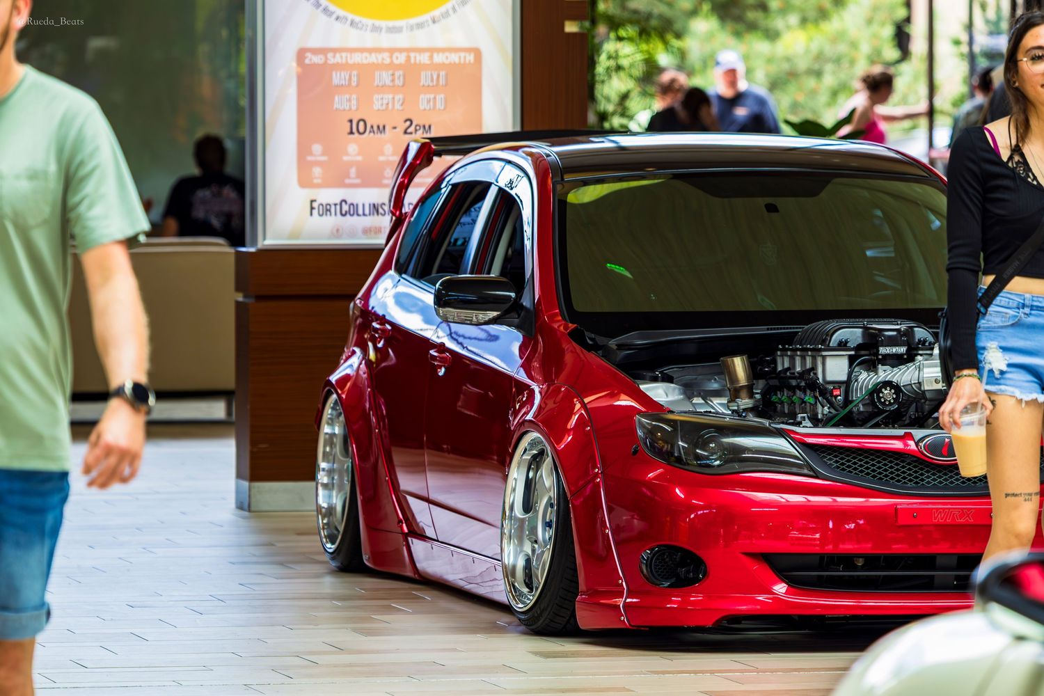 Red slammed custom VW hatchback with hood open displaying engine at an indoor car show.