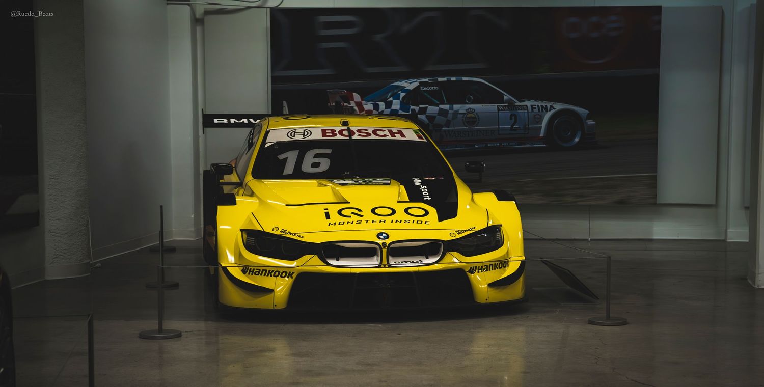 Yellow BMW M4 DTM race car number 16 with iQOO sponsorship displayed in a museum.