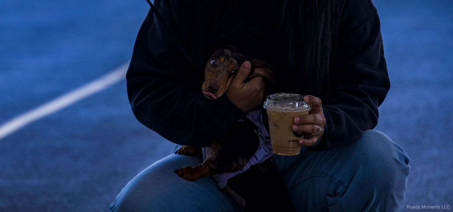 Person sitting outdoors at dusk holding an iced coffee drink in a plastic cup.