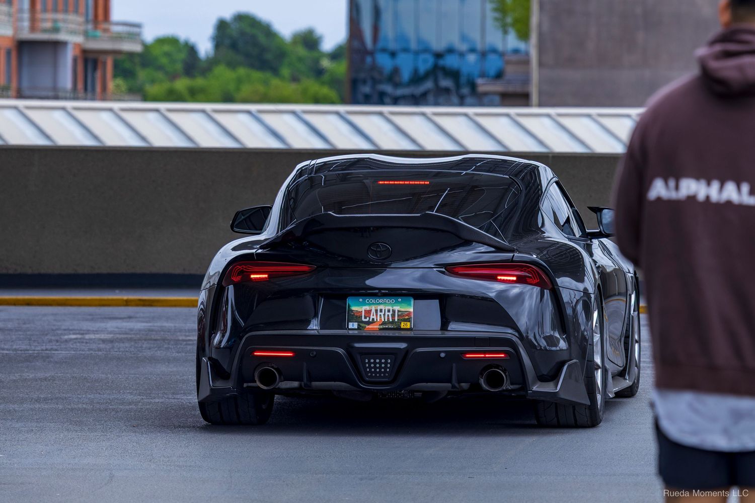 Black Toyota Supra A90 rear view with red taillights in a parking lot at a car meet.