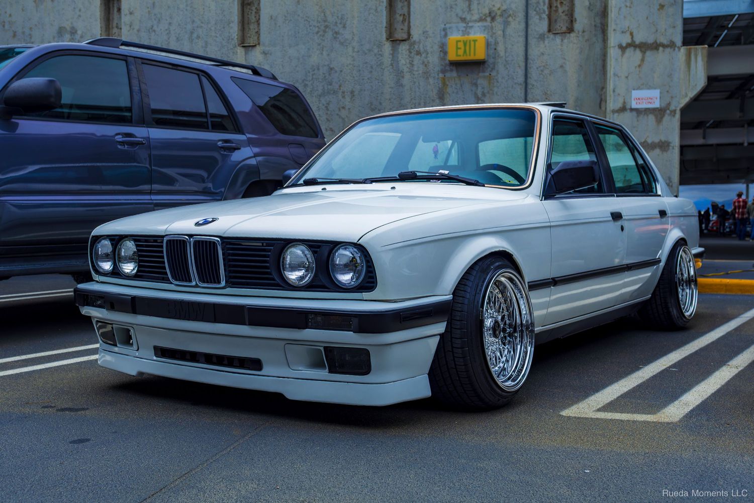 Classic white BMW E30 3 Series on BBS wheels at an outdoor car show.