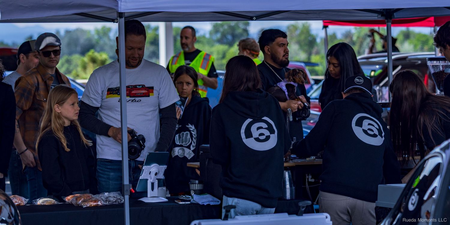 Group of people gathered under a tent at an outdoor automotive community event booth.