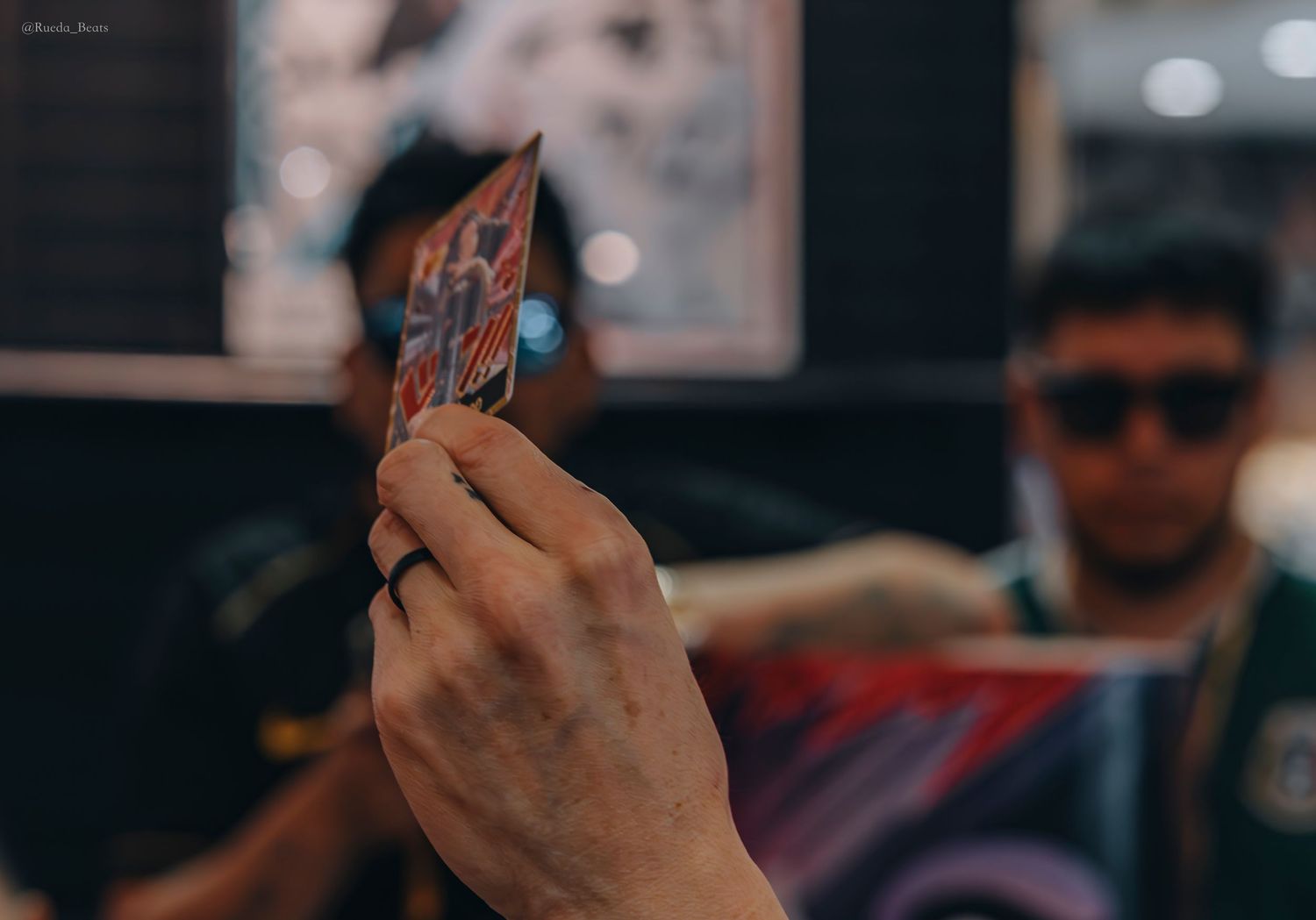 Hand holds colorful trading card with tattooed collector in background.