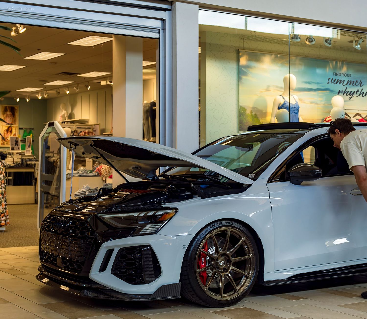 White Audi RS3 with hood open displayed inside a retail store showroom.